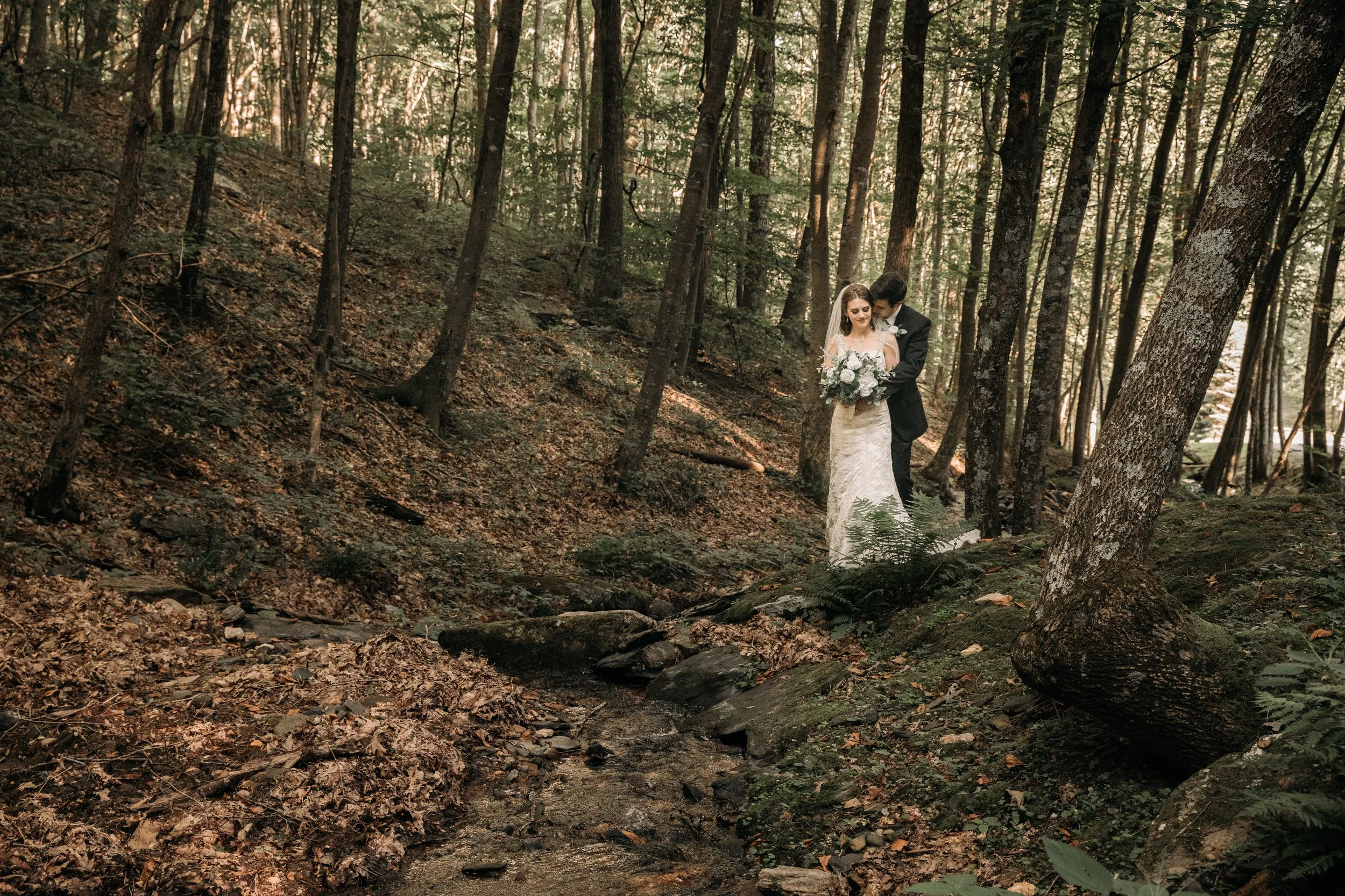 Bride and groom standing together in a wooded creek setting for a romantic mountain wedding portrait.