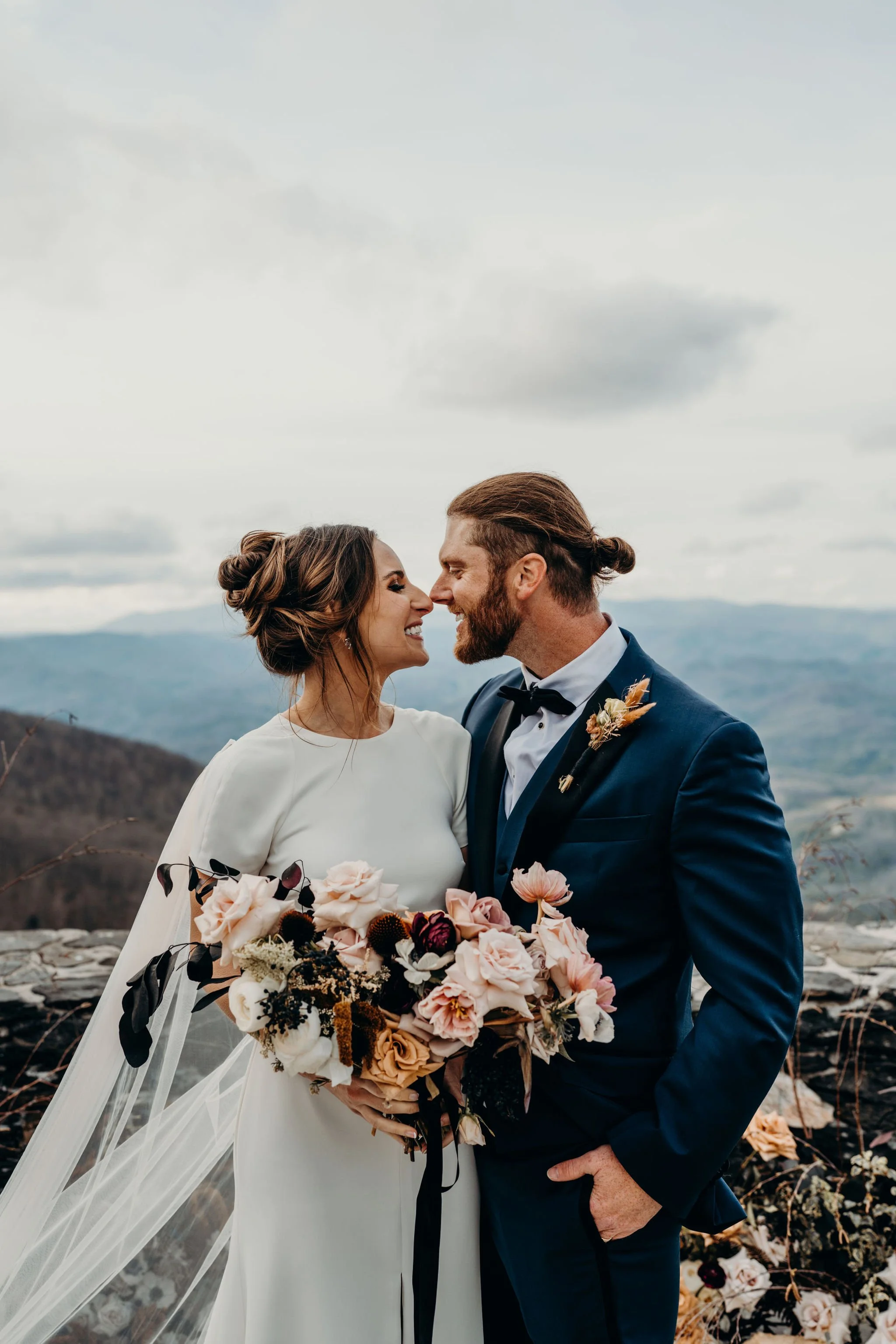 Groom kissing the bride’s forehead during a mountain portrait as she holds her bouquet.