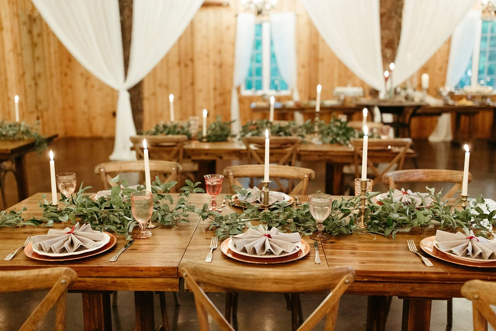 Rustic wedding reception tables with greenery garlands, taper candles, and white draping
