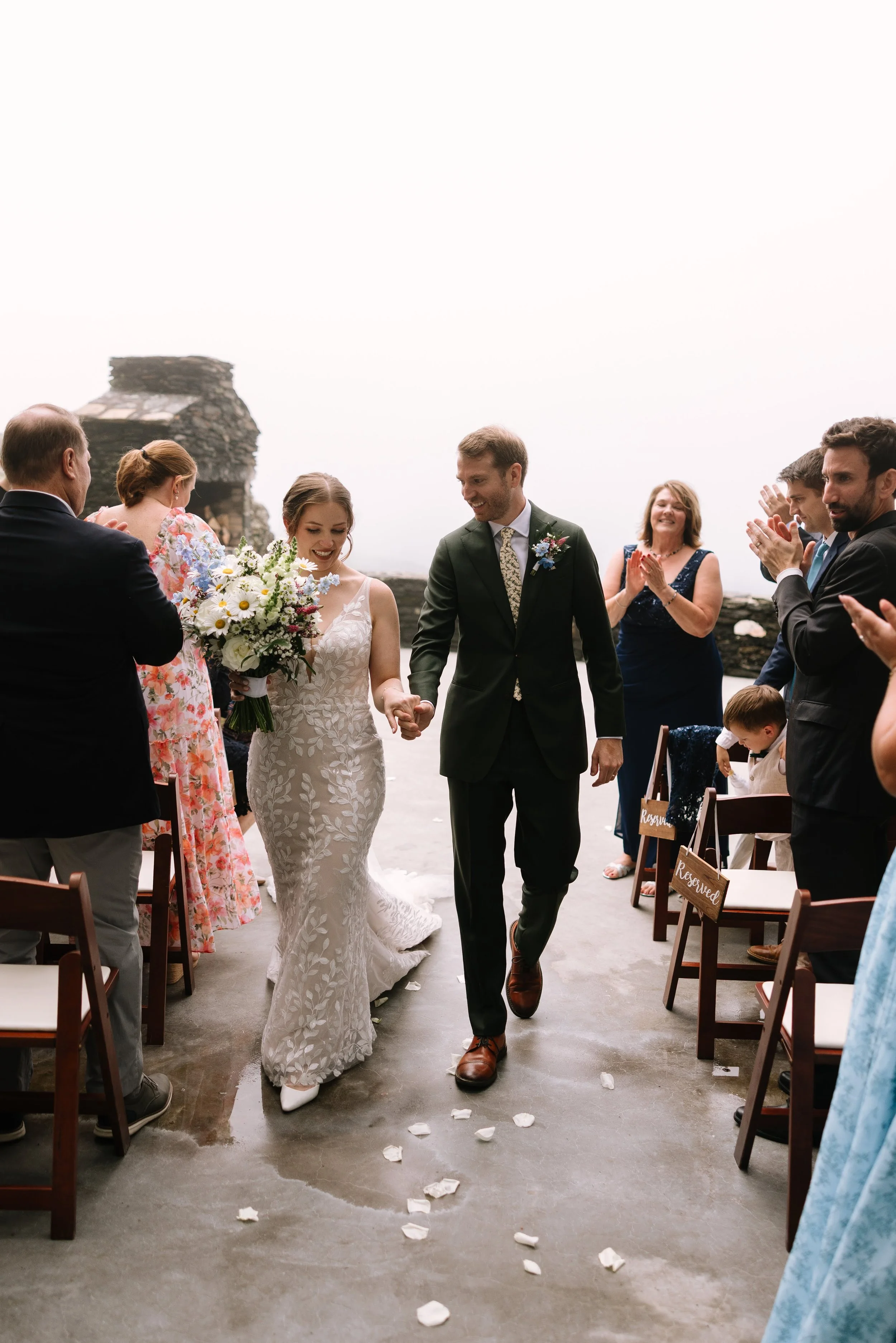 Newlyweds walking hand in hand down the aisle after their outdoor mountain wedding ceremony.