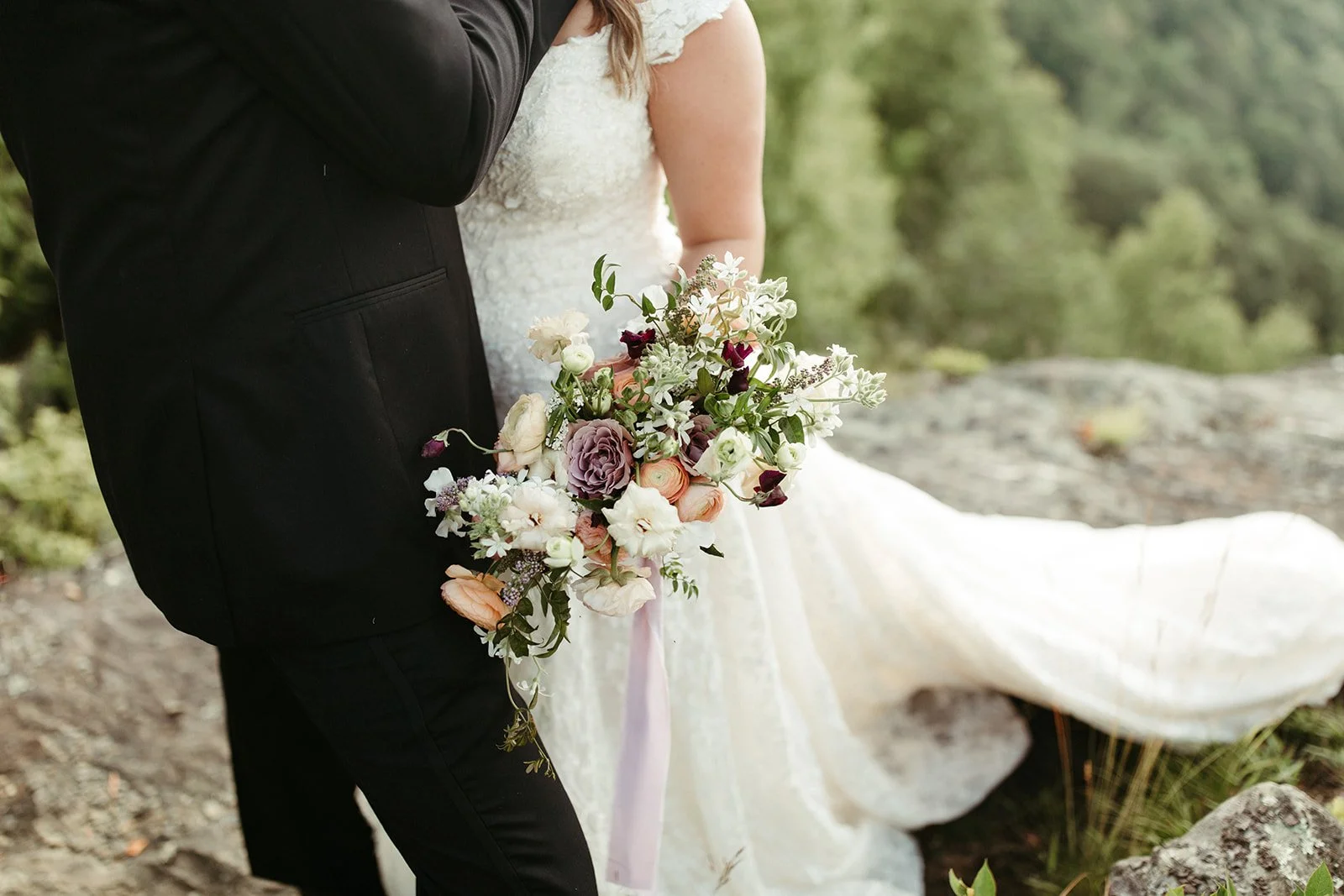 Closeup of the bride holding a garden-style bouquet during mountain portraits, lace dress visible.