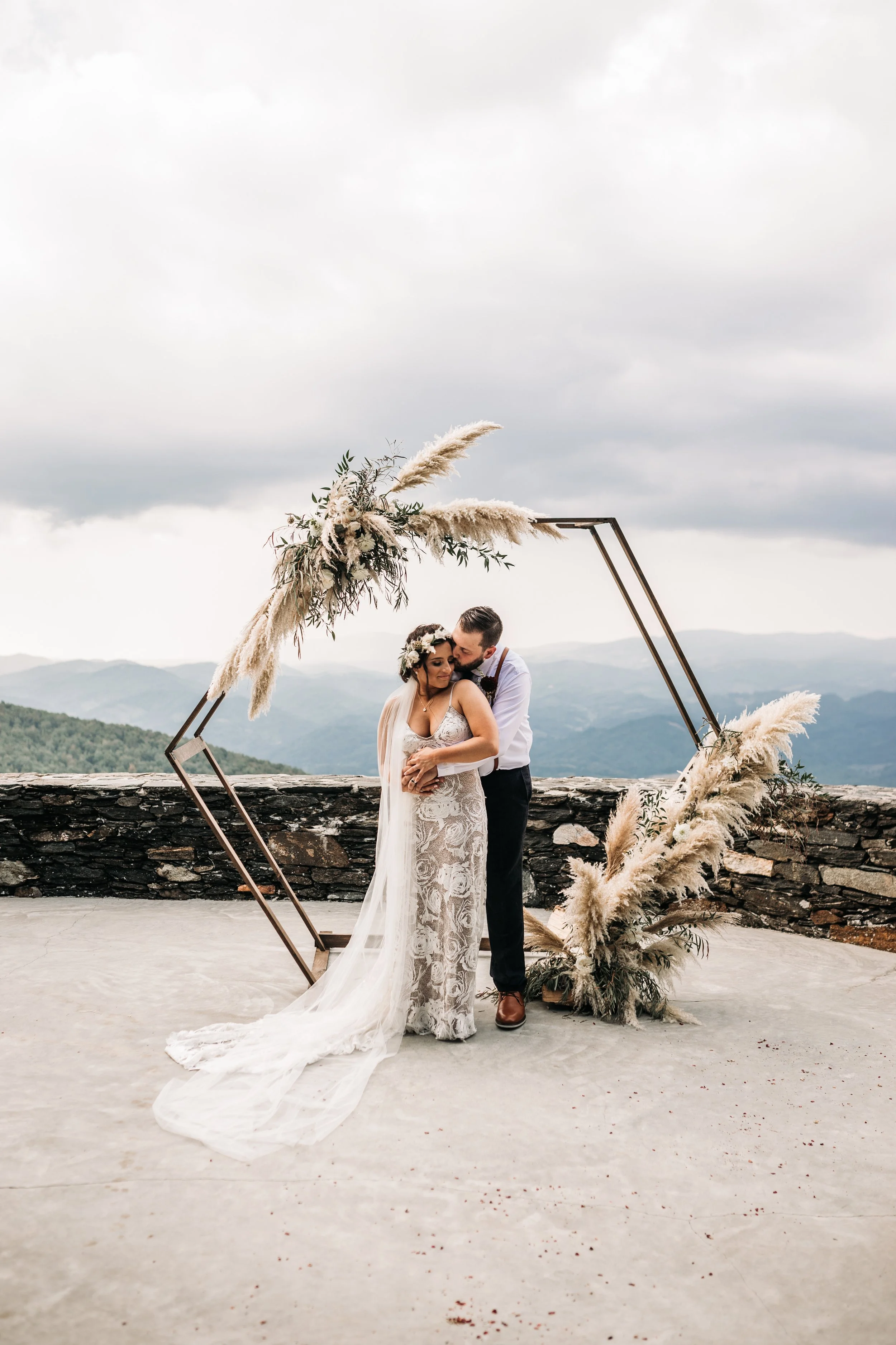 Wide shot of a mountain ceremony with the couple standing beneath a hexagon arch with pampas grass.
