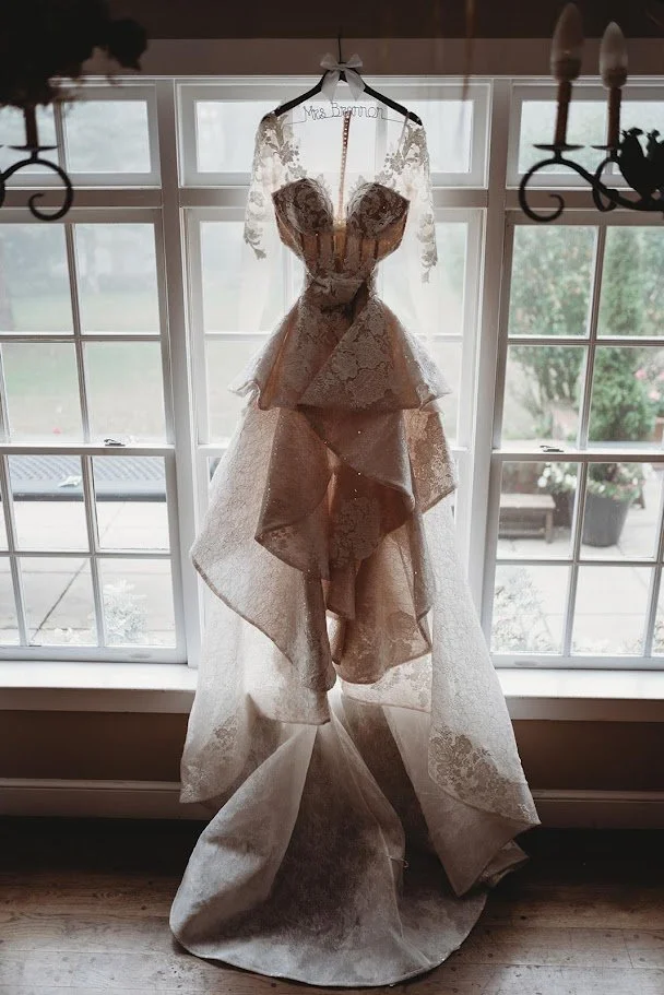 Lace wedding dress hanging in front of a large window in a bridal suite.
