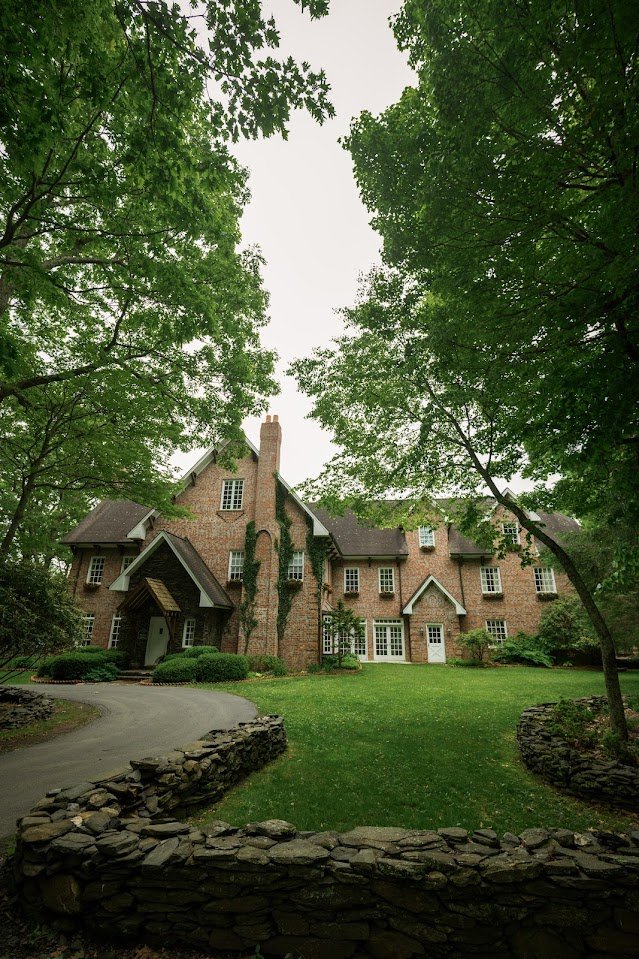 Brick estate house exterior framed by trees and a green lawn.