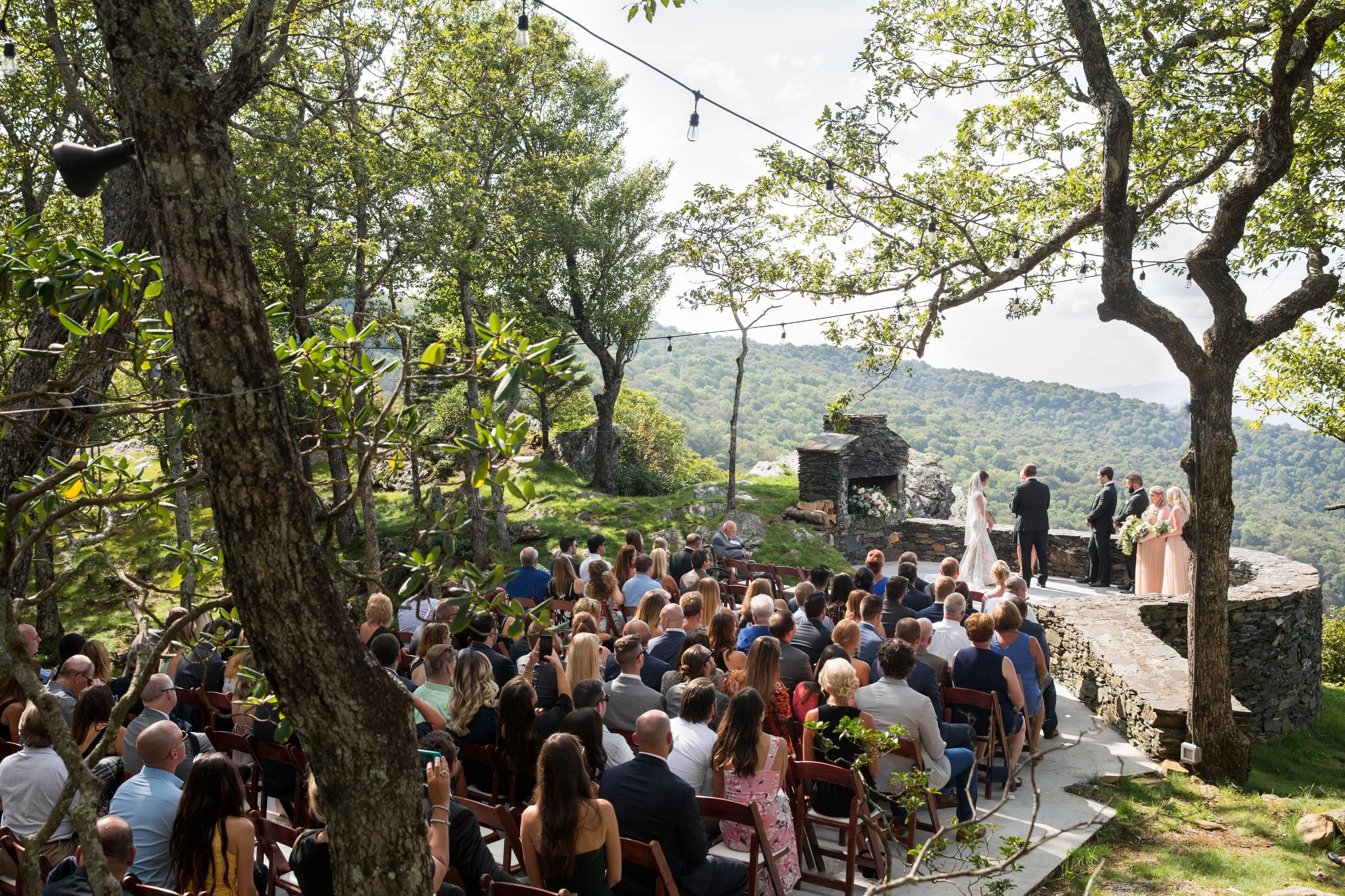 Wide view of a mountain wedding ceremony at a stone overlook with seated guests.
