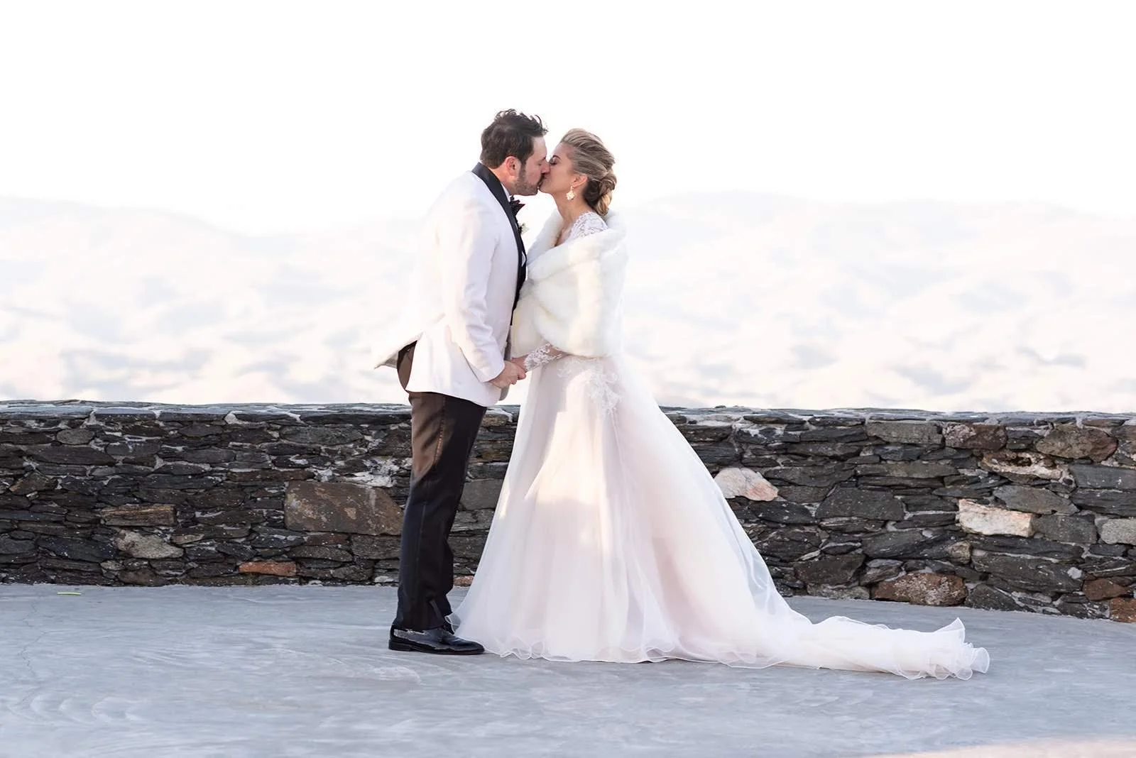 Bride and groom kissing outdoors on a winter overlook in formal attire.