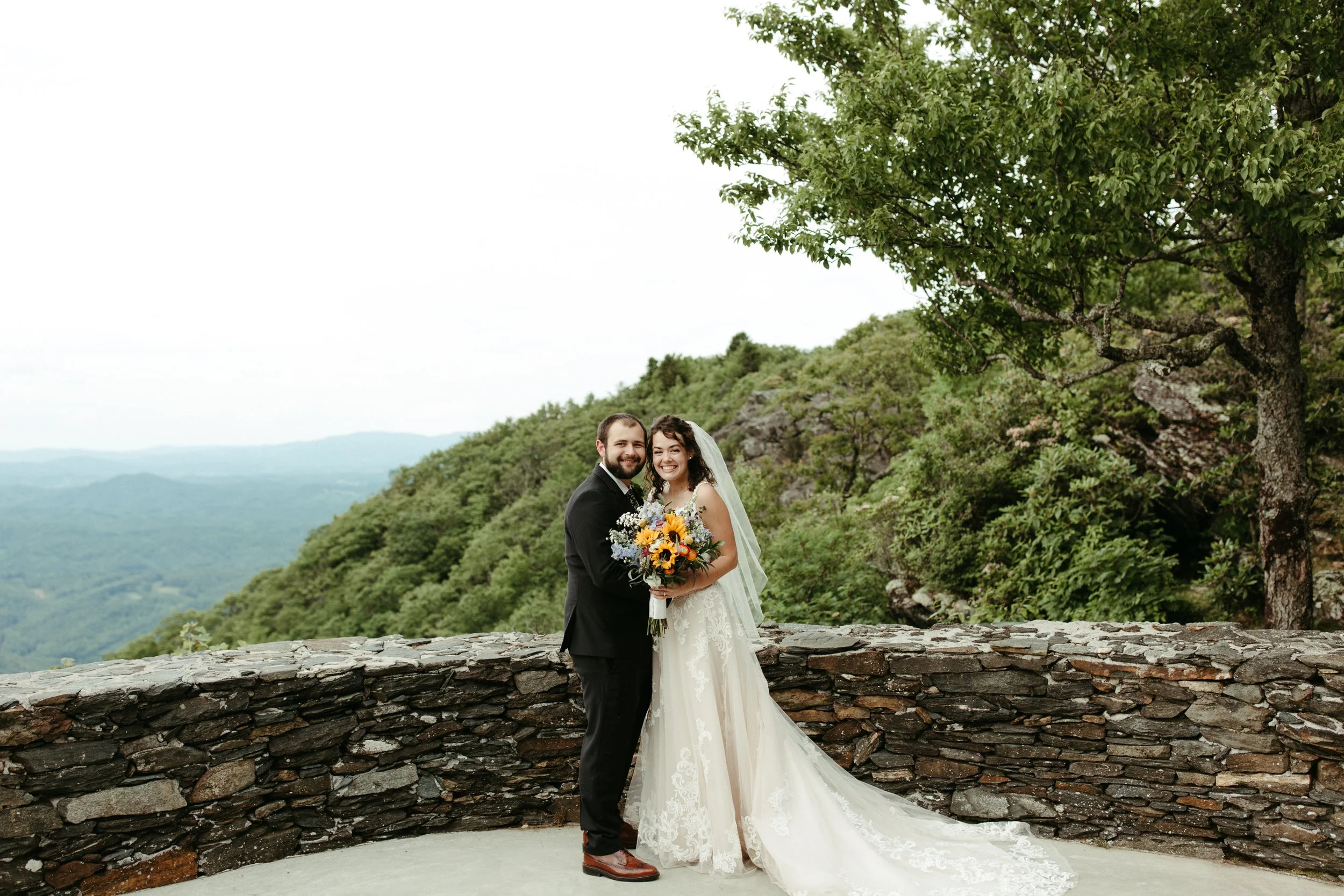 Bride and groom standing by a stone wall for a mountain overlook wedding portrait.