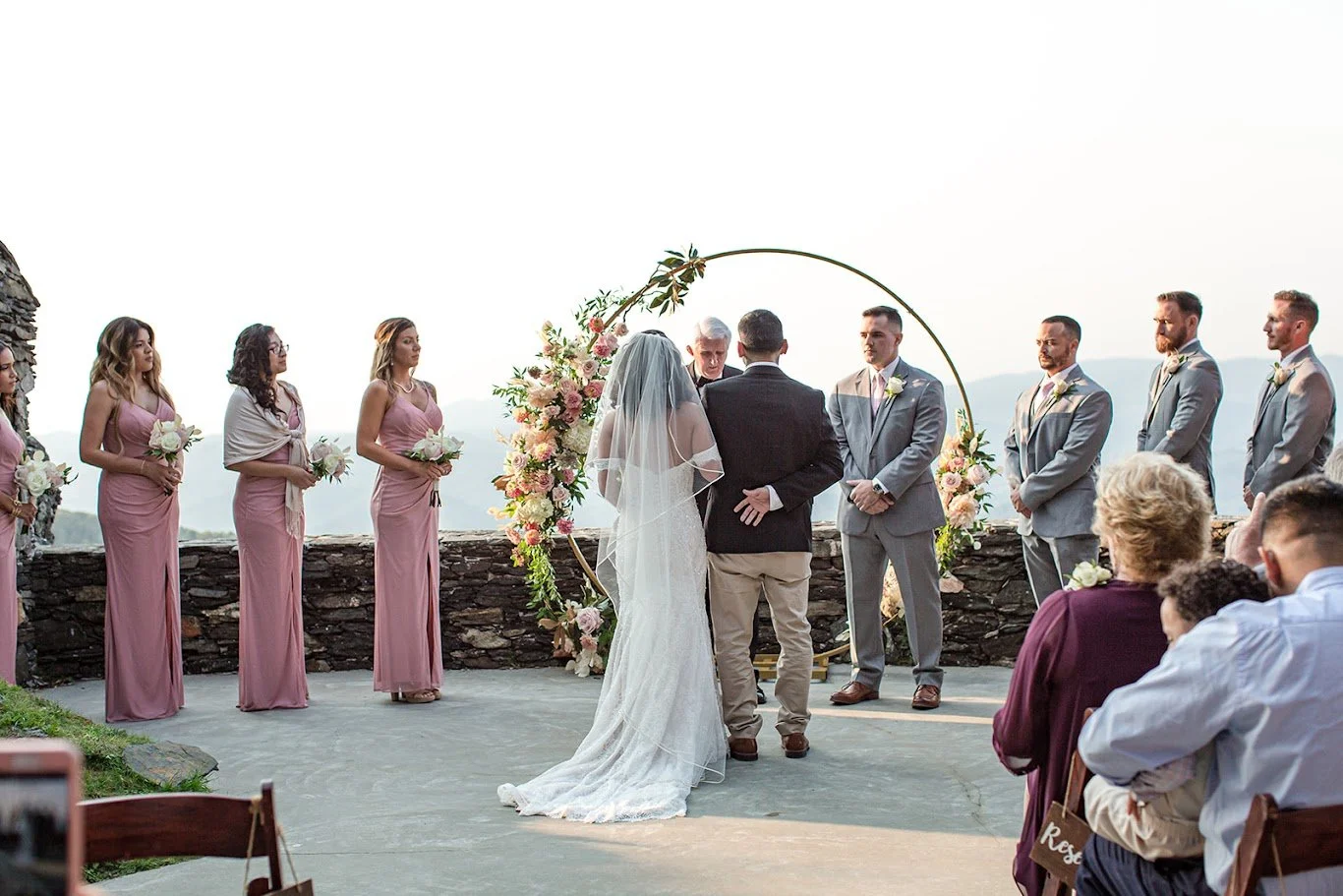 Rear view of the couple during a mountain wedding ceremony under a circular floral arch