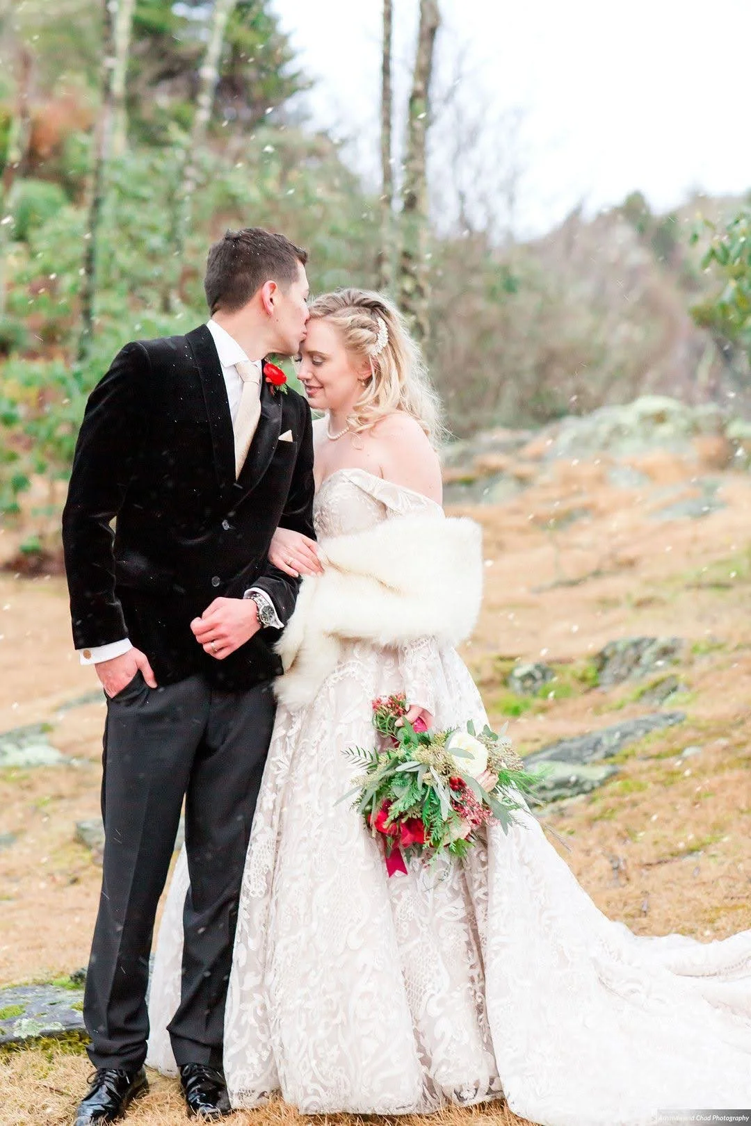 Bride and groom embracing outdoors in light snow, bride wearing a fur wrap and holding a winter bouquet.