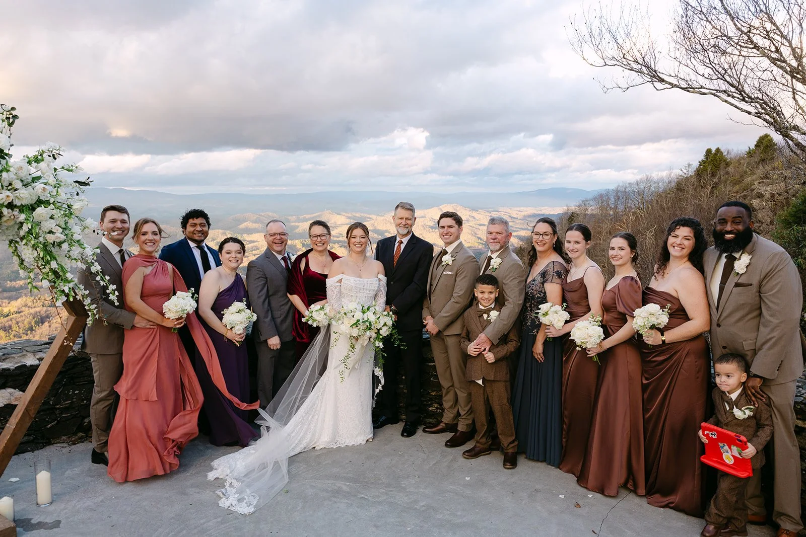 Wedding family formal portrait at a mountain overlook with the couple centered and guests smiling.