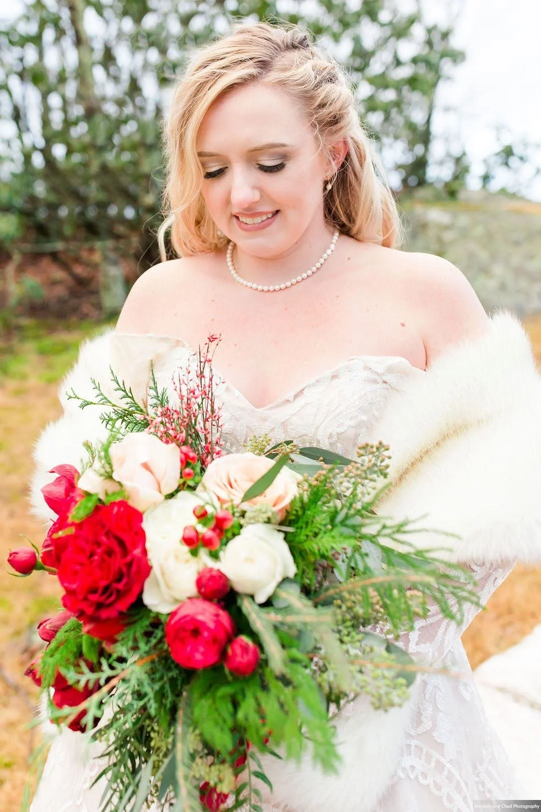 Bride smiling while holding a winter bouquet with red and white flowers, wearing a fur wrap.