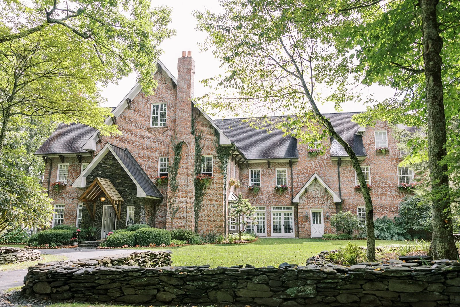 Brick estate wedding venue exterior surrounded by trees and a stone wall on a sunny day
