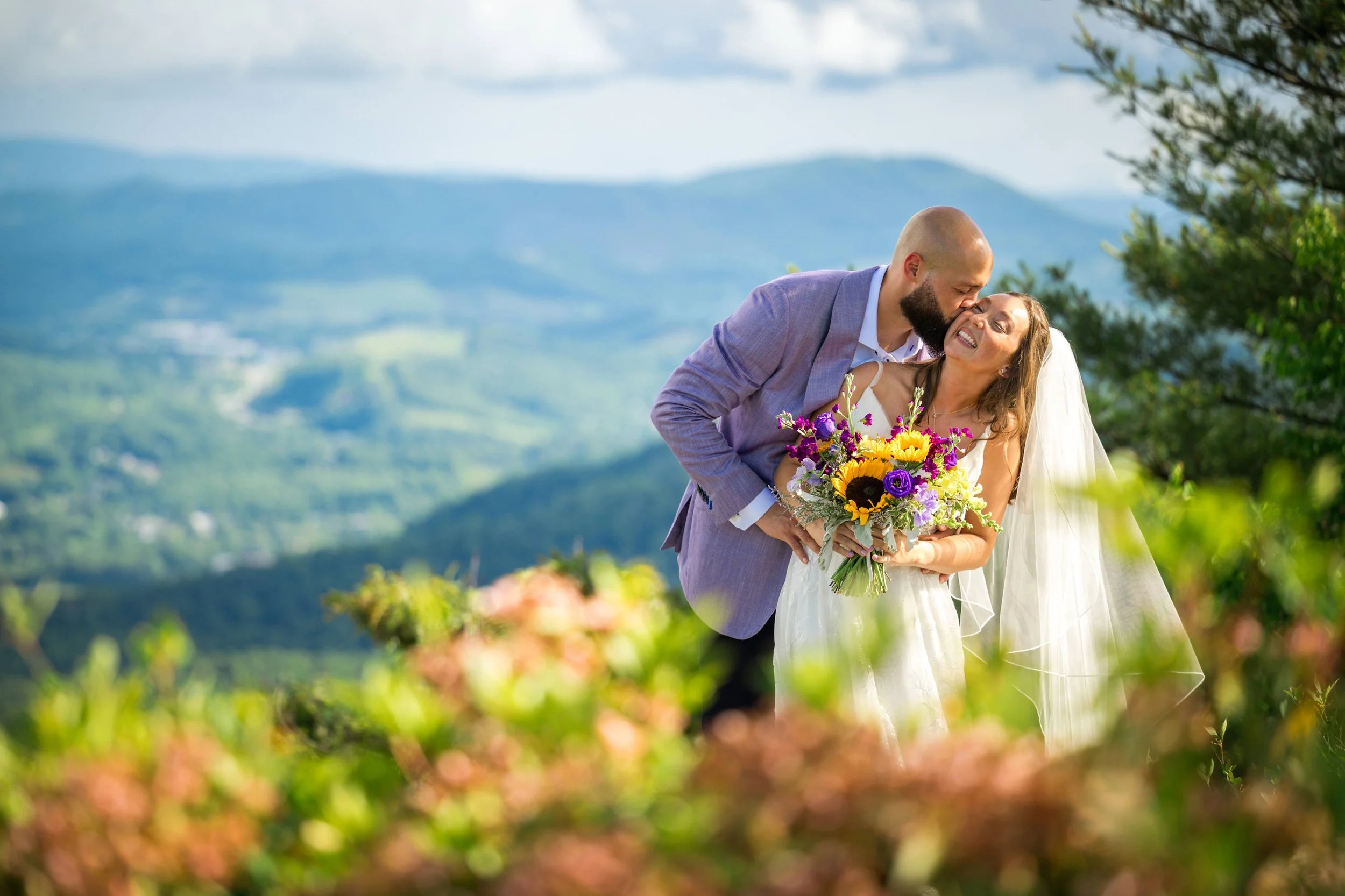 Romantic bride and groom portrait in the mountains with colorful bouquet, wedding veil, and scenic valley views