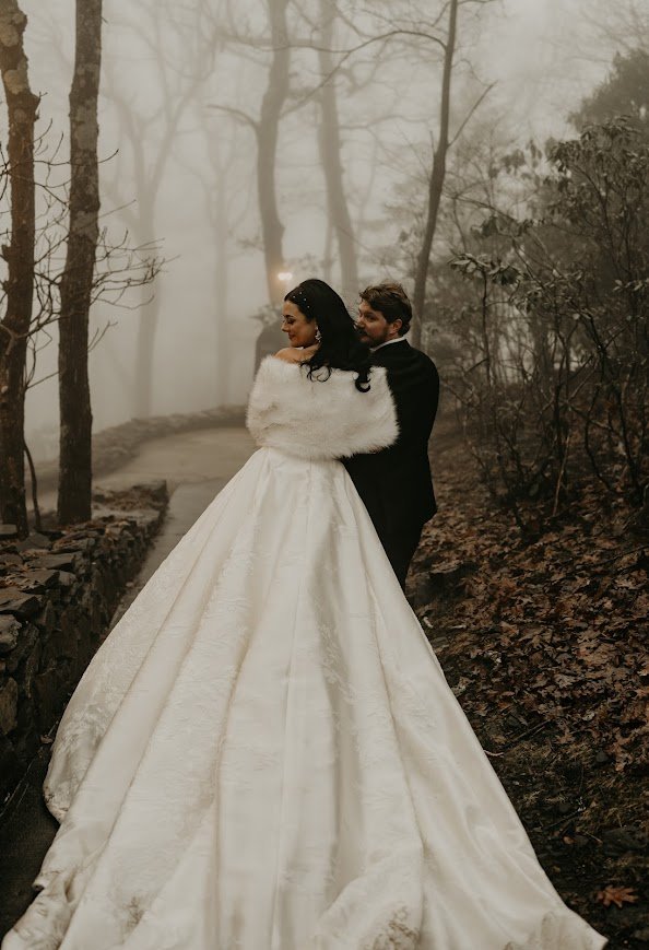 Bride in a fur wrap with a long gown in a foggy forest wedding portrait.