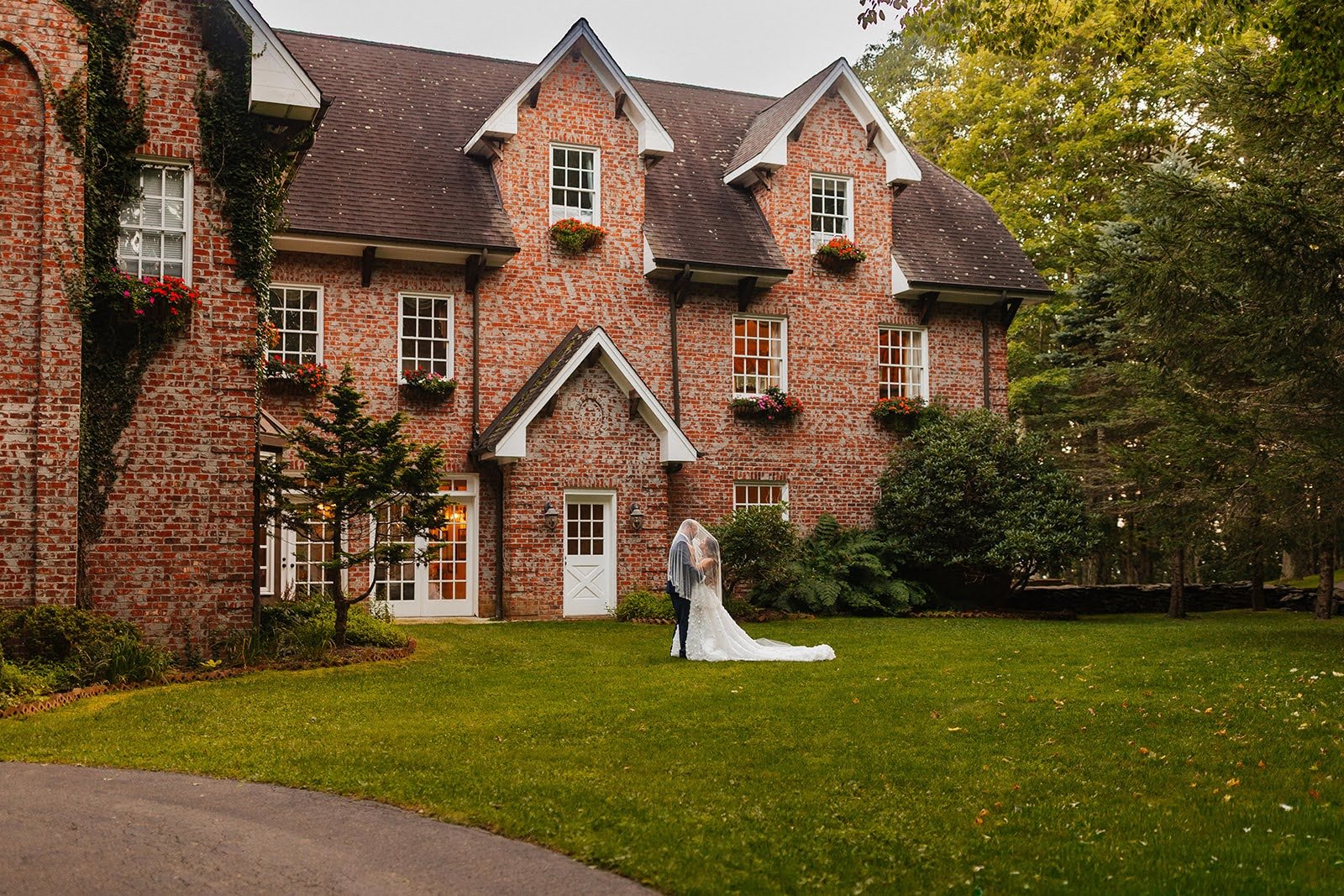 Bride and groom standing on the lawn outside a historic brick estate wedding venue with ivy and greenery.