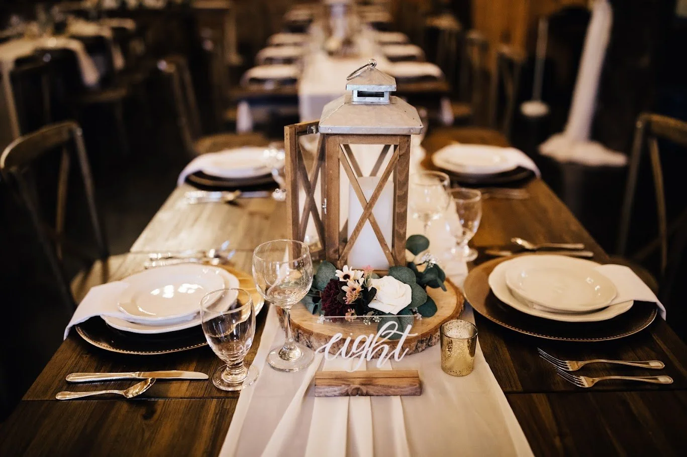 Closeup of a wedding reception table setting with a lantern centerpiece and white runner.