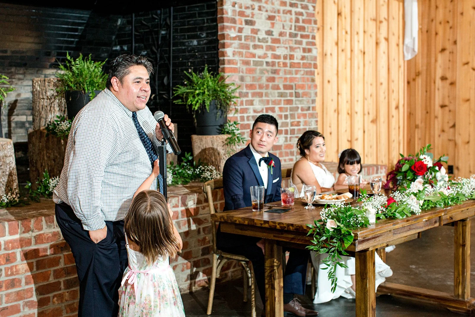 Guest giving a speech at a rustic barn wedding reception while the couple sits at the head table.