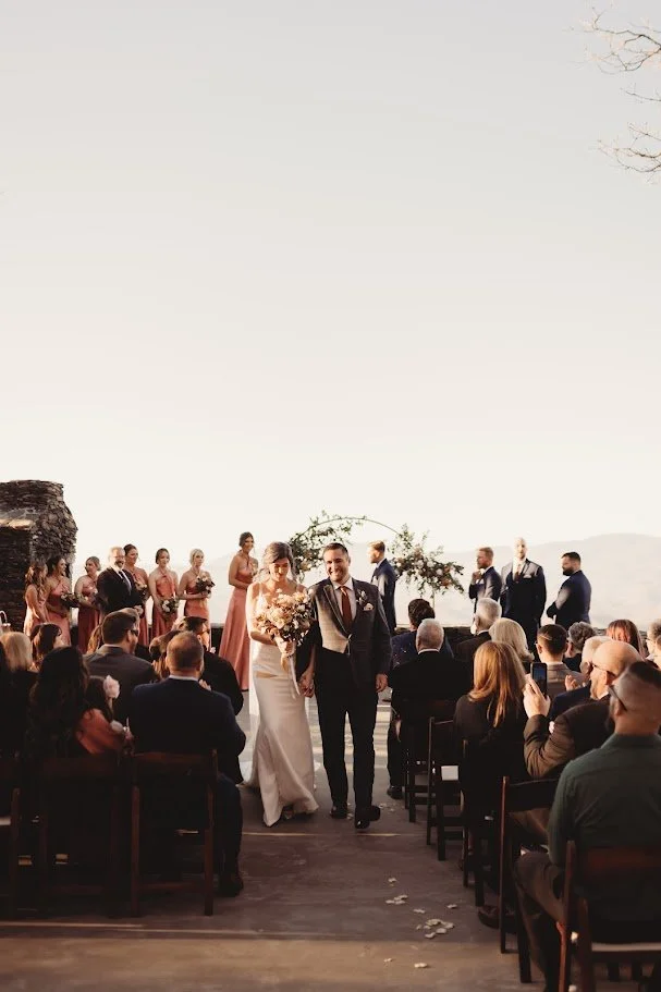 Bride and groom walking back down the aisle after a mountaintop ceremony with guests seated on both sides