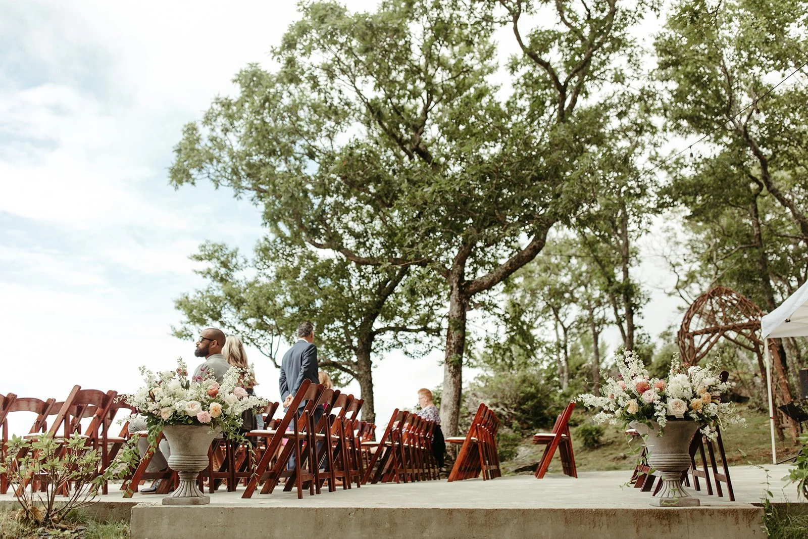 Outdoor wedding ceremony setup with wooden chairs and large floral urns at a mountain venue.