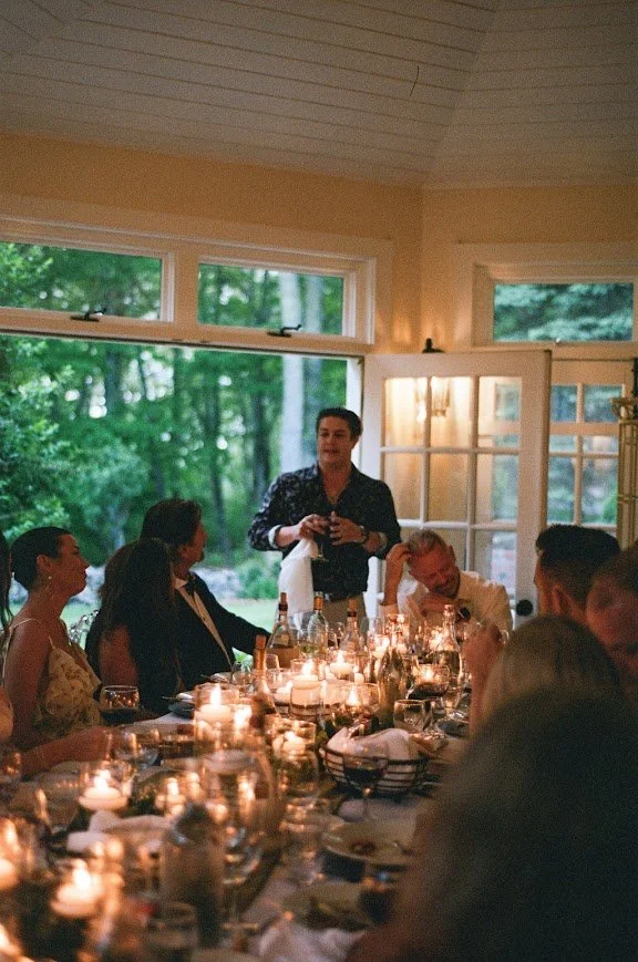 Candlelit dinner reception indoors with a guest giving a toast at a long table