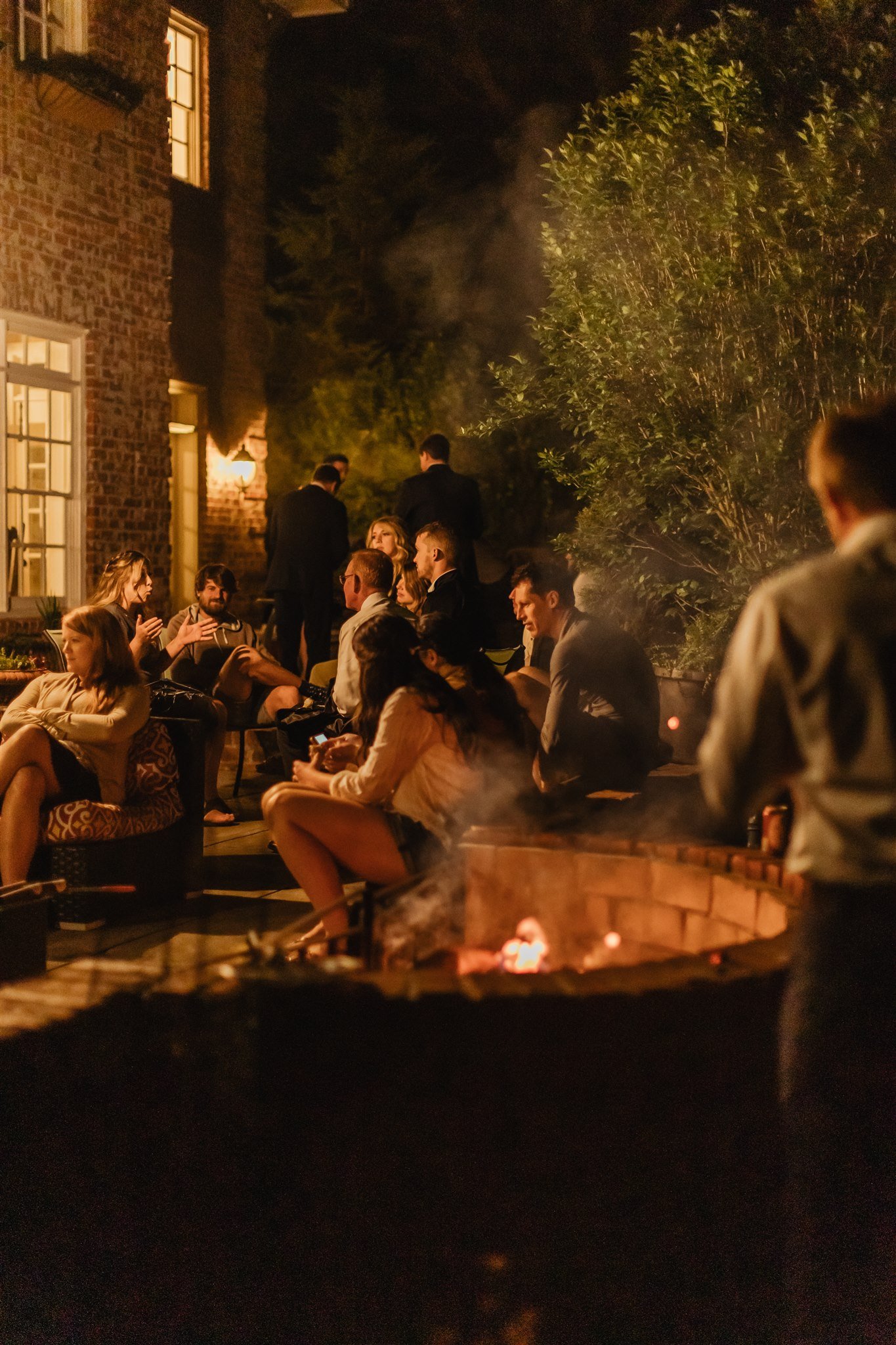 Wedding guests gathered around a fire pit outdoors at night during the after-party