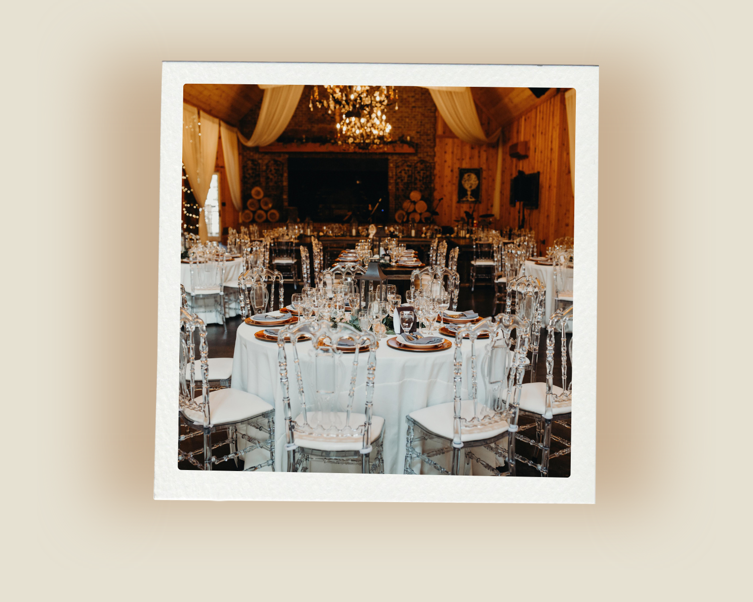 Rustic barn wedding reception with round tables, clear chairs, chandeliers, and white draping