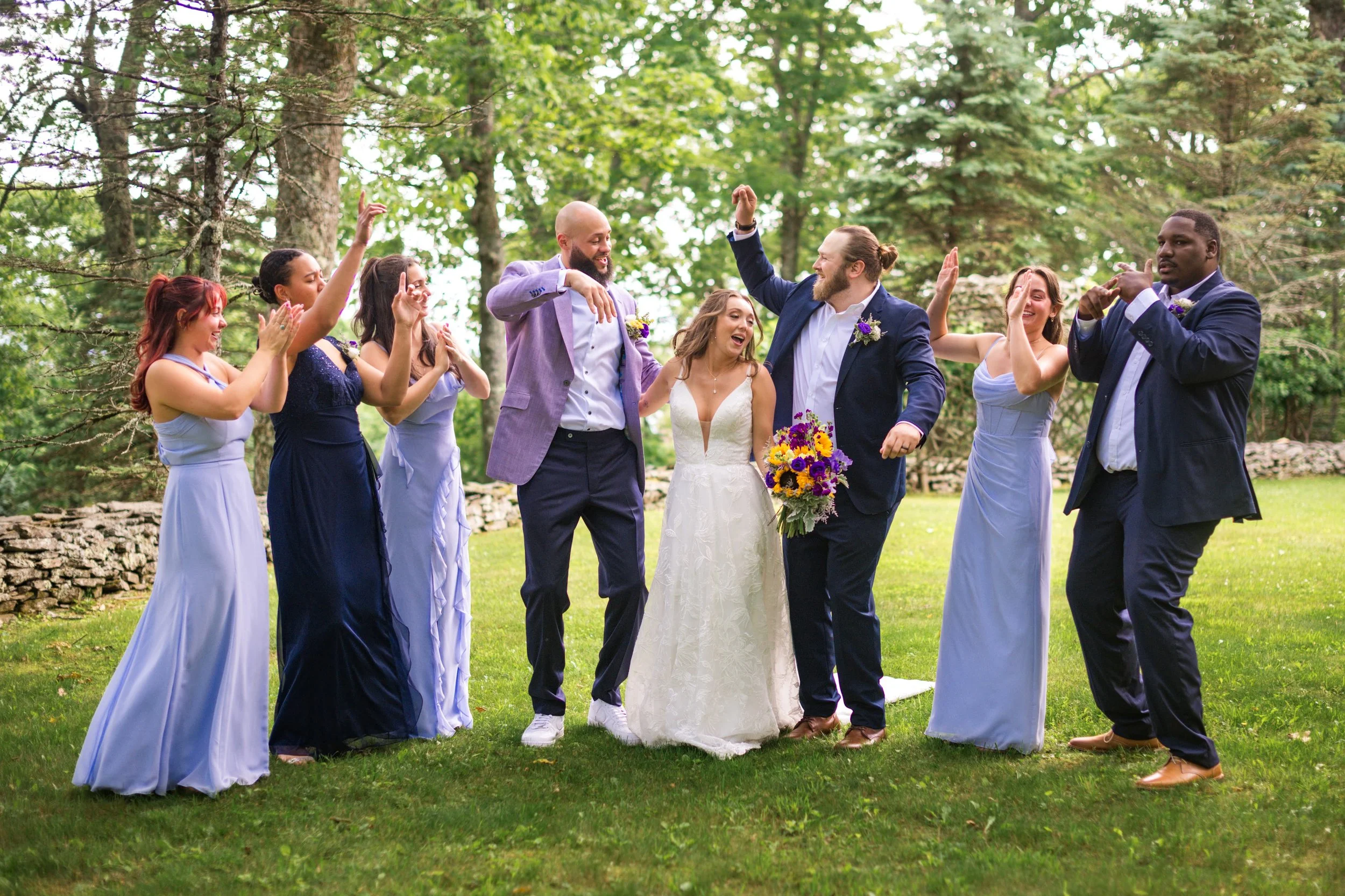 Bride, groom, bridesmaids, and groomsmen celebrating together at an outdoor forest wedding venue