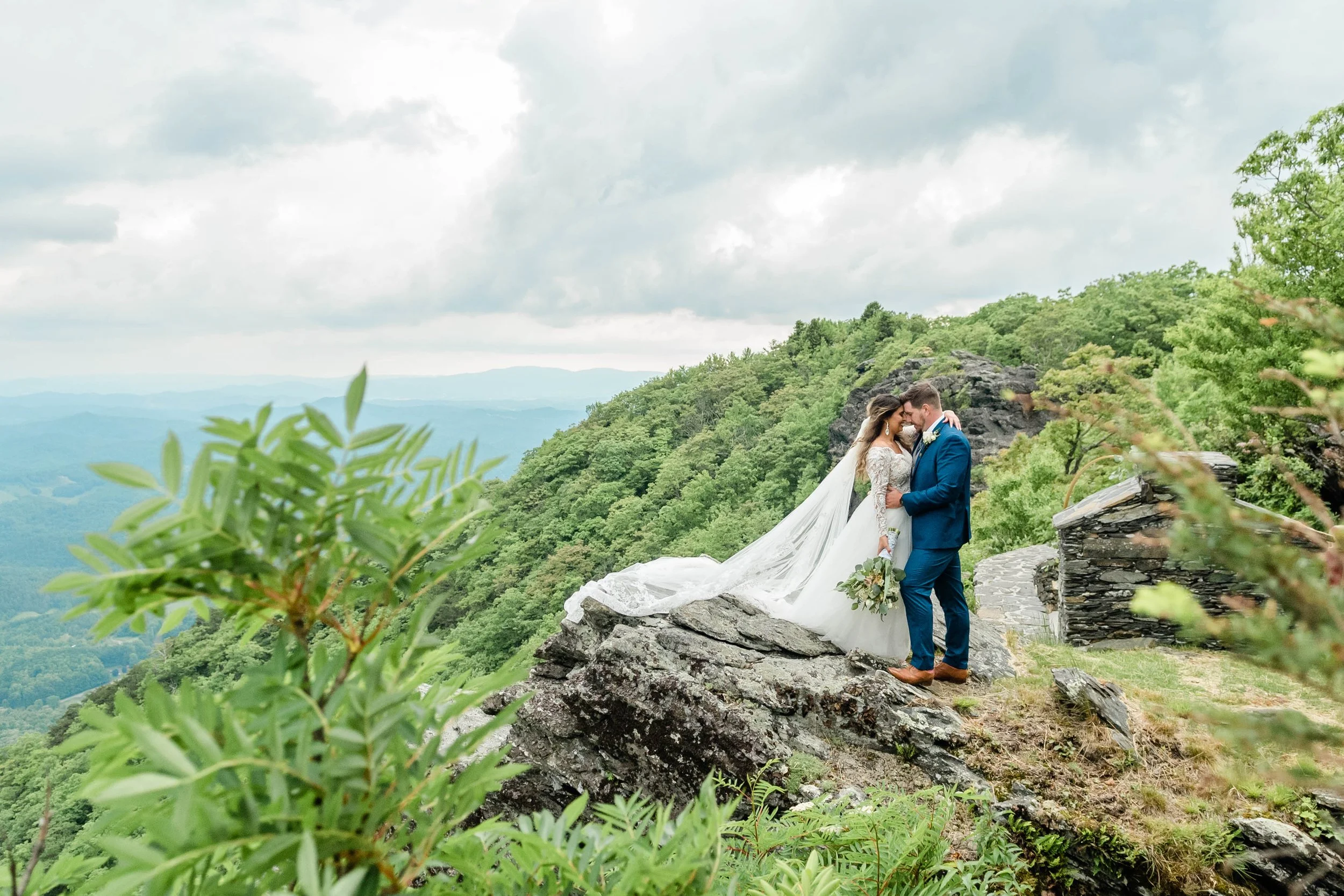 Bride and groom kissing on a rocky mountain overlook with the bride’s long veil spread out behind