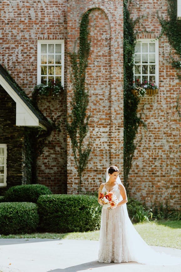 Bride holding a bouquet standing in front of an ivy-covered brick wall at Twickenham House & Hall