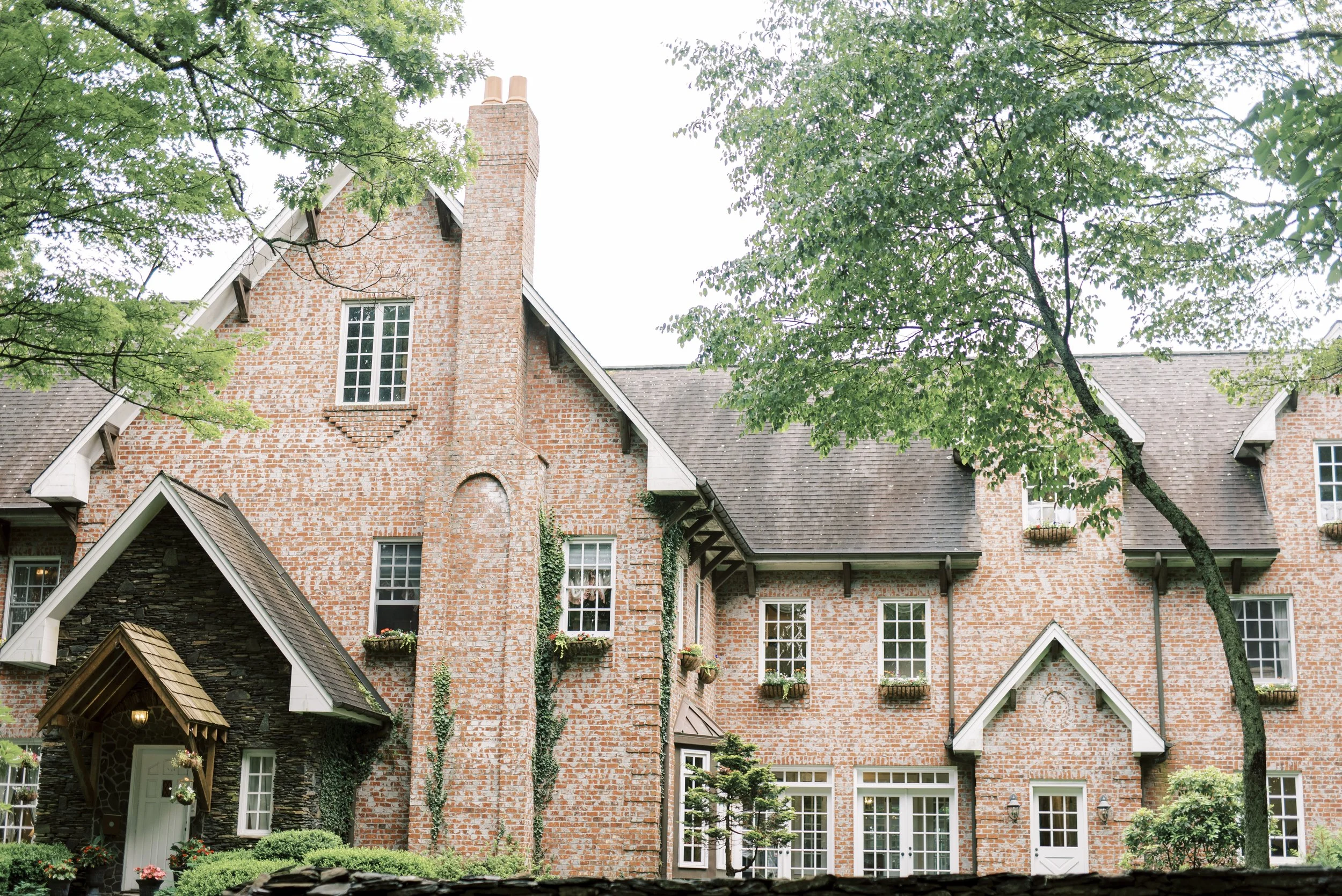 Brick estate wedding venue exterior surrounded by green trees and landscaping on a bright day