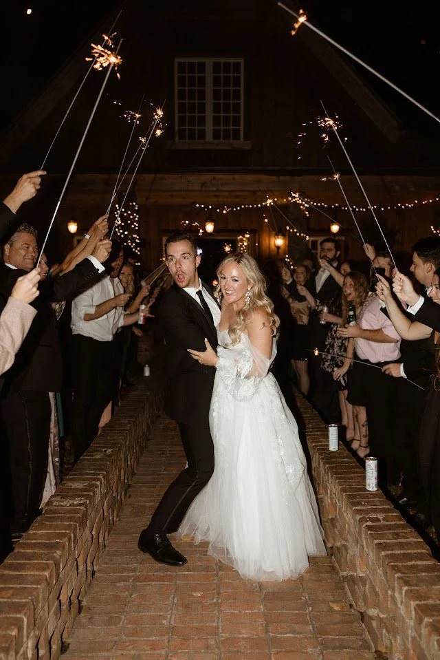 Wedding couple posing during a nighttime sparkler exit with guests lining the walkway.