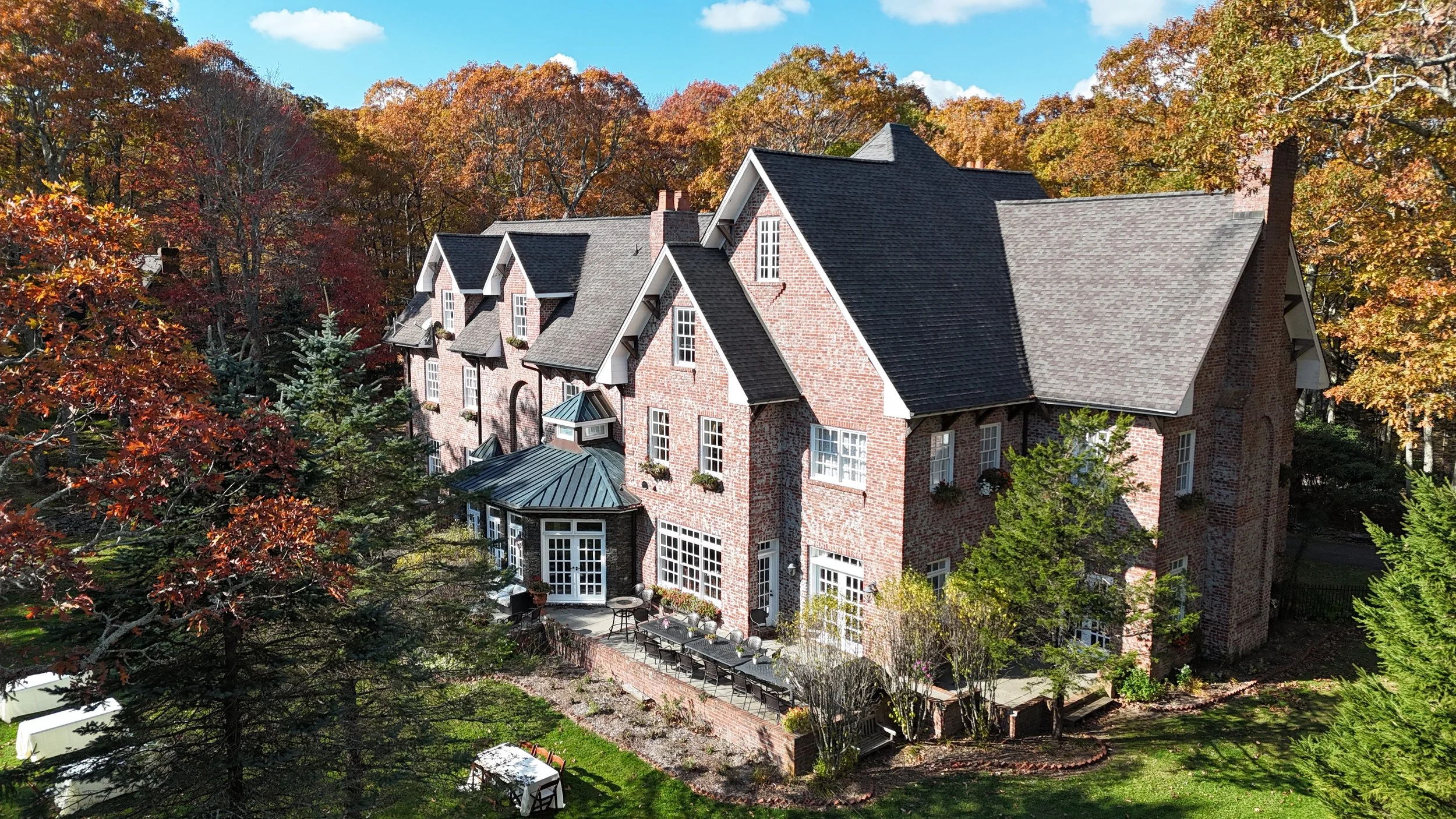 Brick manor front facade framed by golden fall branches, showing the entryway, windows, and lawn in sunlight.