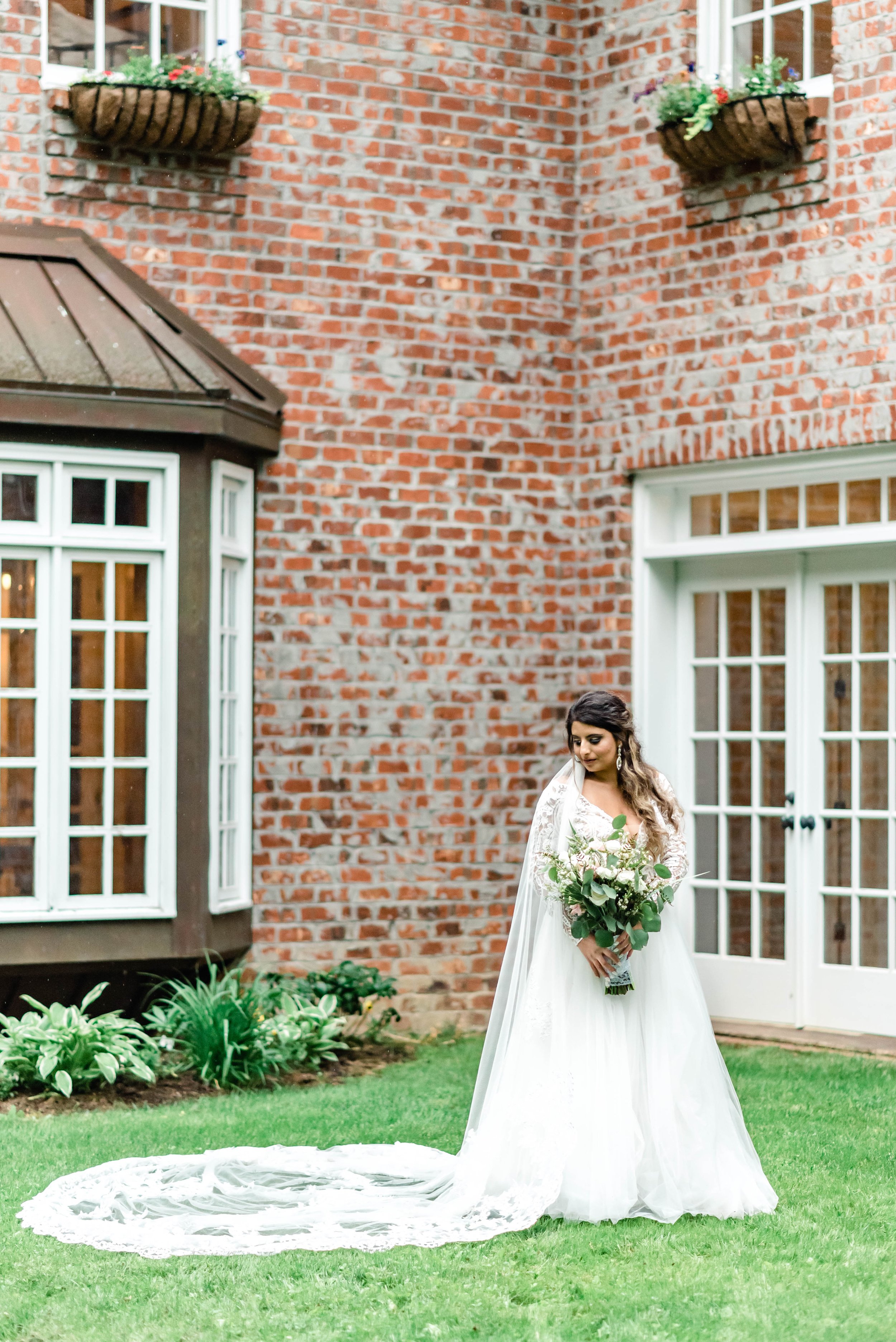Bride standing outside a brick estate wedding venue in a lace wedding dress with a long veil.