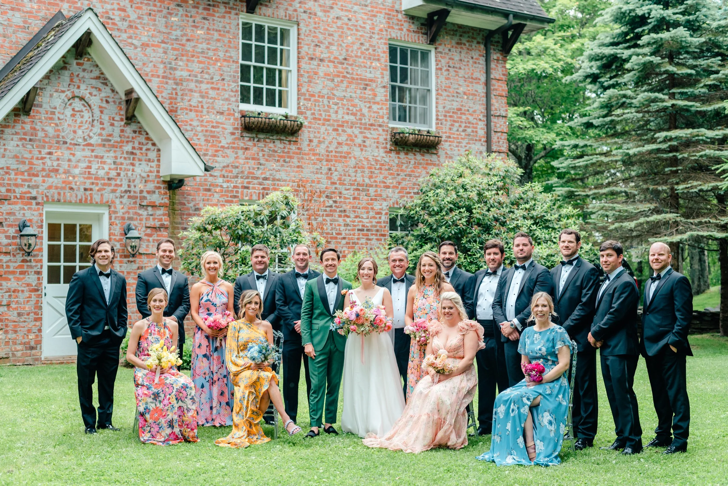 Bride and groom posing with their colorful wedding party outside a historic brick estate wedding venue.