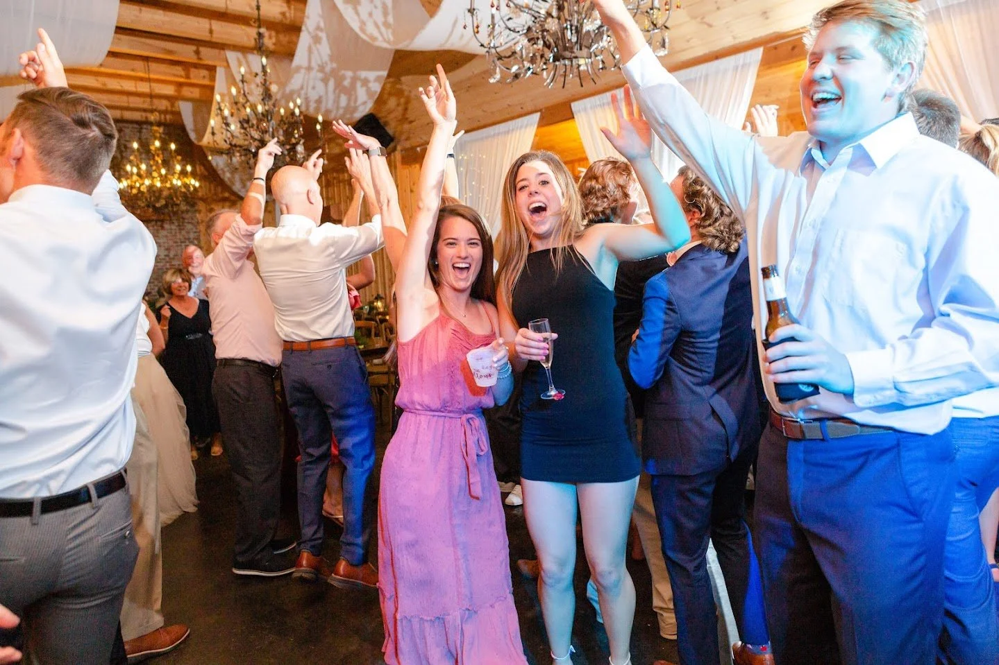 Wedding guests dancing with hands up during a high-energy reception.