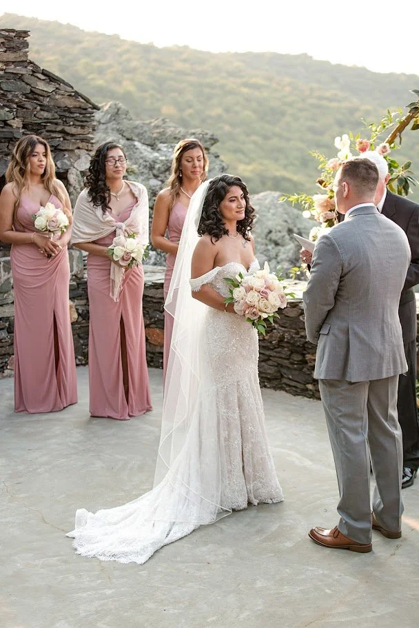 Bride in an off-the-shoulder wedding gown with a long veil holding a blush-and-white rose bouquet