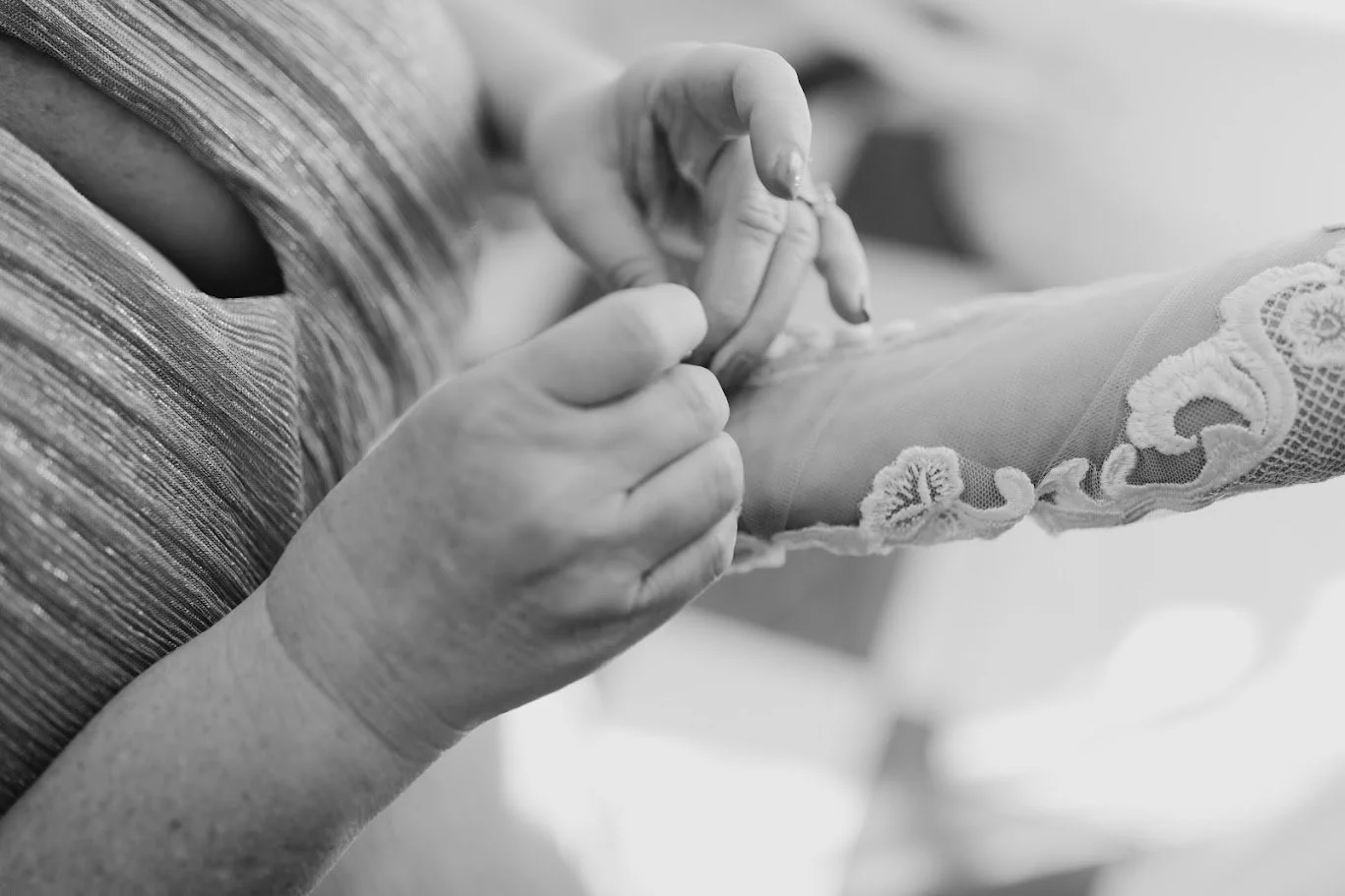 Black and white close-up of hands fastening a wedding detail during getting-ready moments.