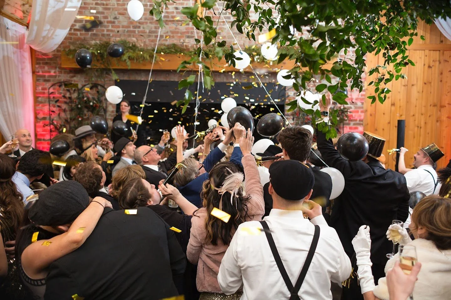 Wedding guests celebrating under black and white balloons with confetti in the air.