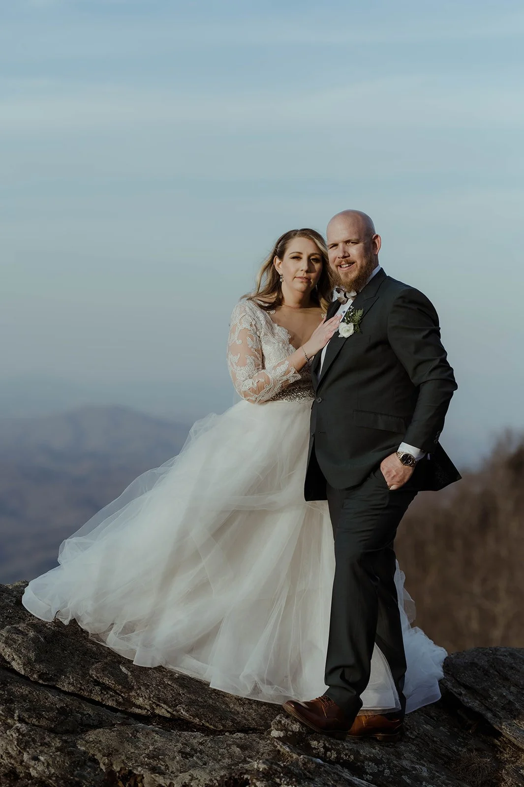 Bride and groom standing together for a romantic portrait with soft Blue Ridge mountain views behind them.
