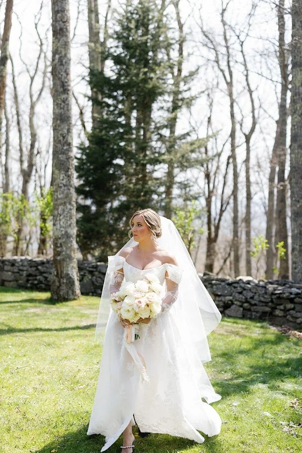 Bride standing on a grassy lawn in a white gown and veil holding a white rose bouquet