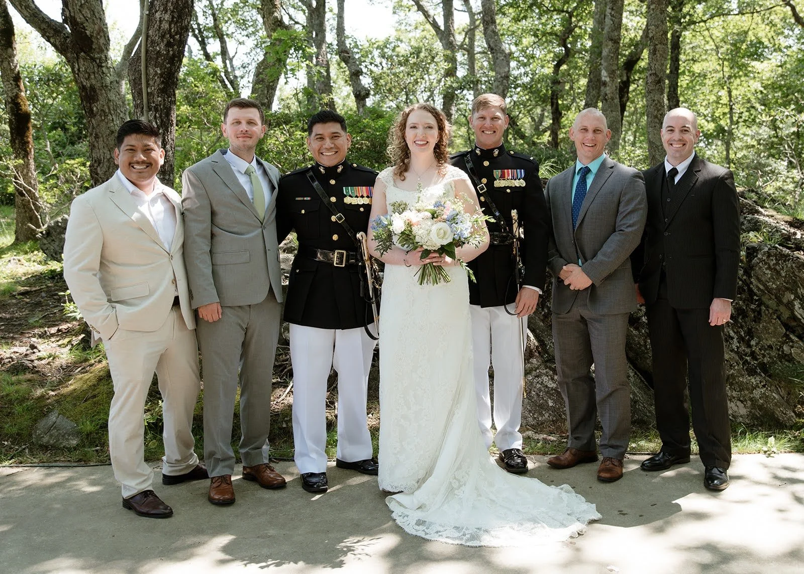 Bride and military groom posing with their wedding party in a wooded outdoor setting