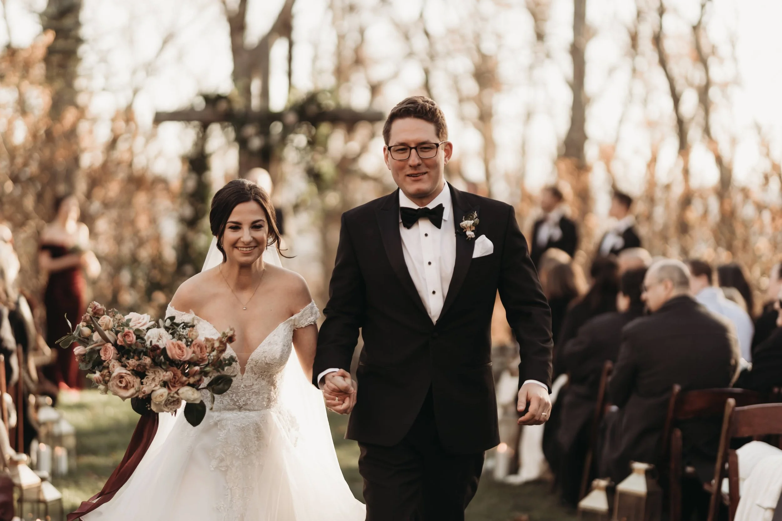 Bride and groom walking down the aisle after the ceremony as guests look on outdoors.