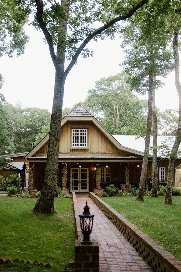 Rustic wood cabin entrance with a brick walkway and trees.