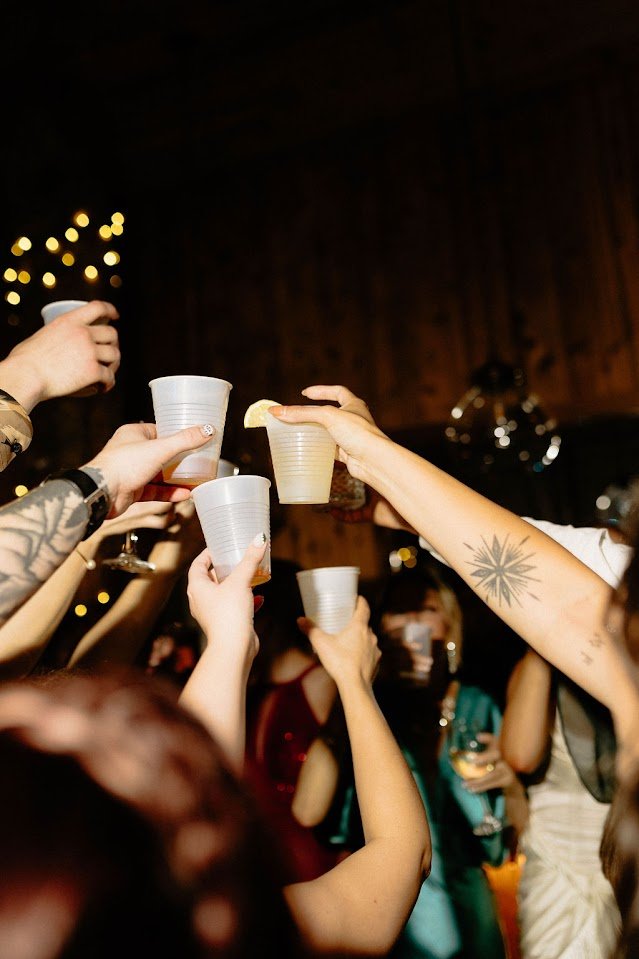 Wedding reception toast with guests clinking plastic cups in a crowd.