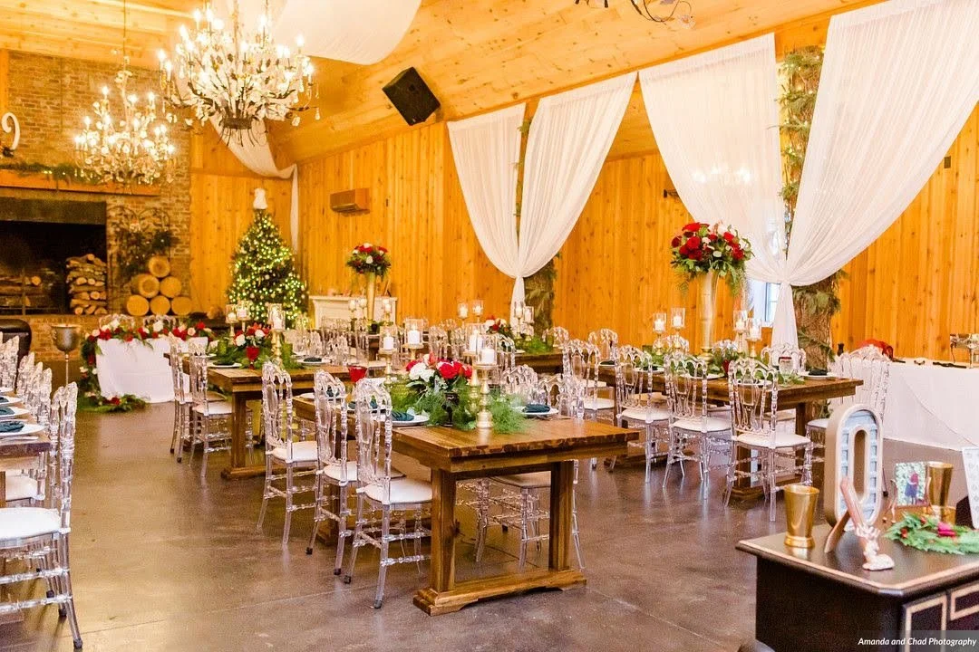 Rustic winter wedding reception with wooden walls, white draping, chandeliers, and long banquet tables.