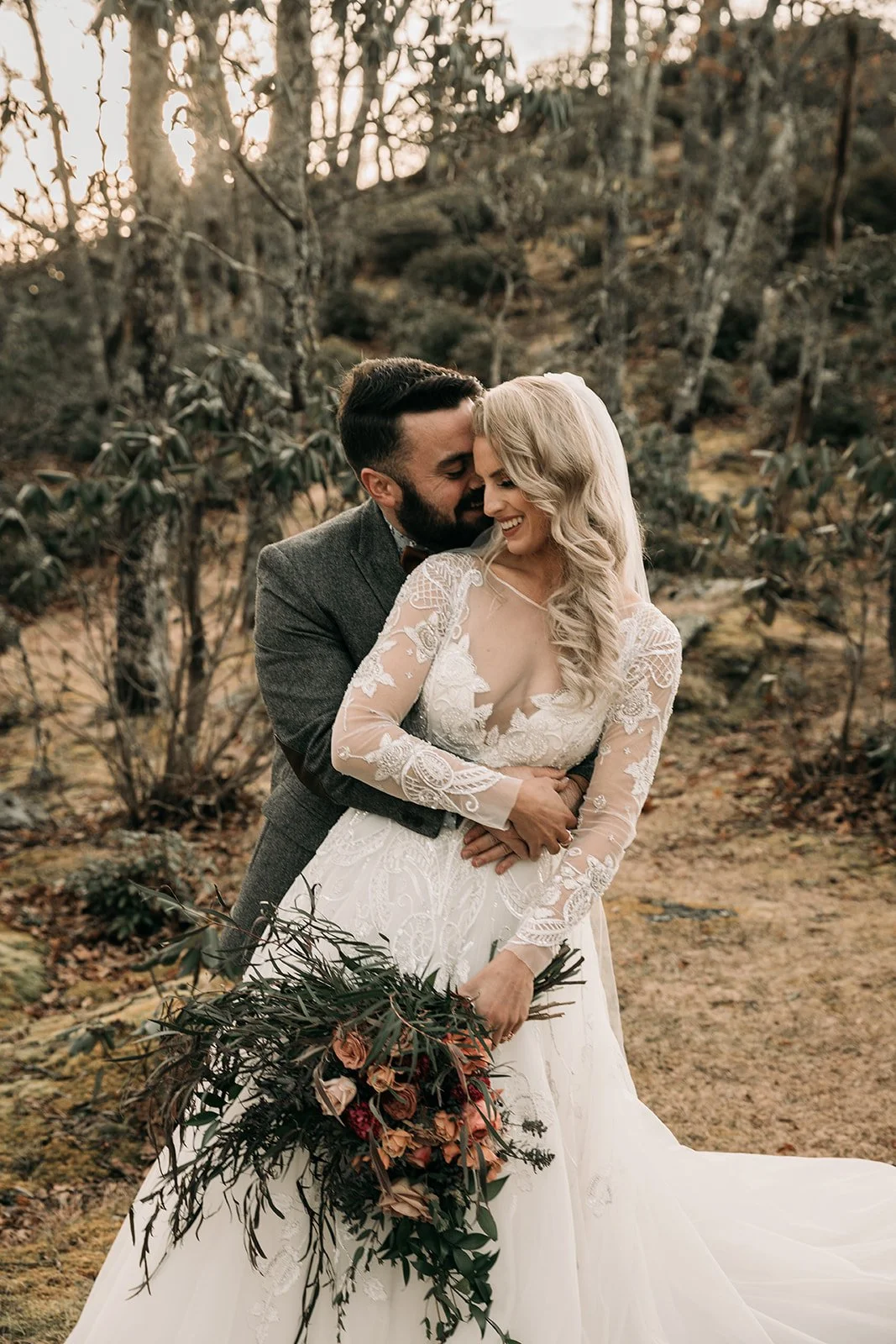 Bride and groom embracing and smiling in a romantic woodland wedding portrait.