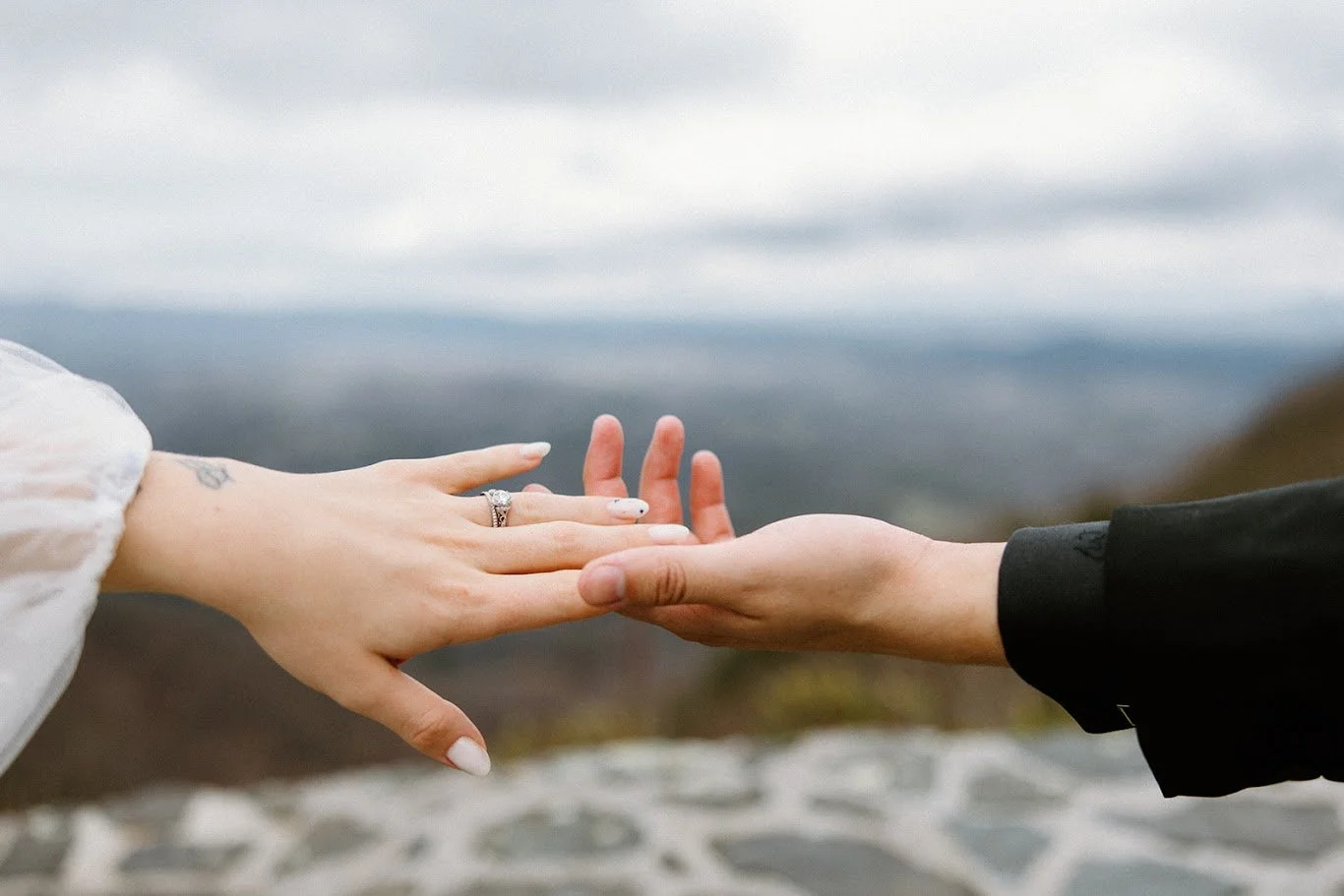 Close-up of the bride and groom reaching hands together, showing the bride’s engagement ring with mountains in the background
