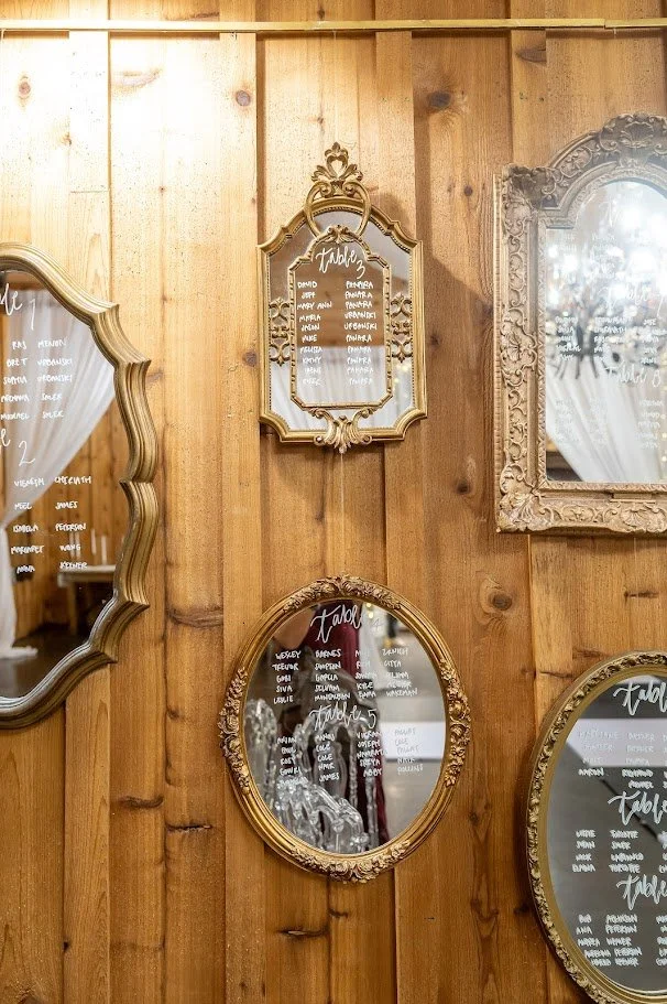 Ornate framed mirrors on a wooden wall display table assignments written in white script.