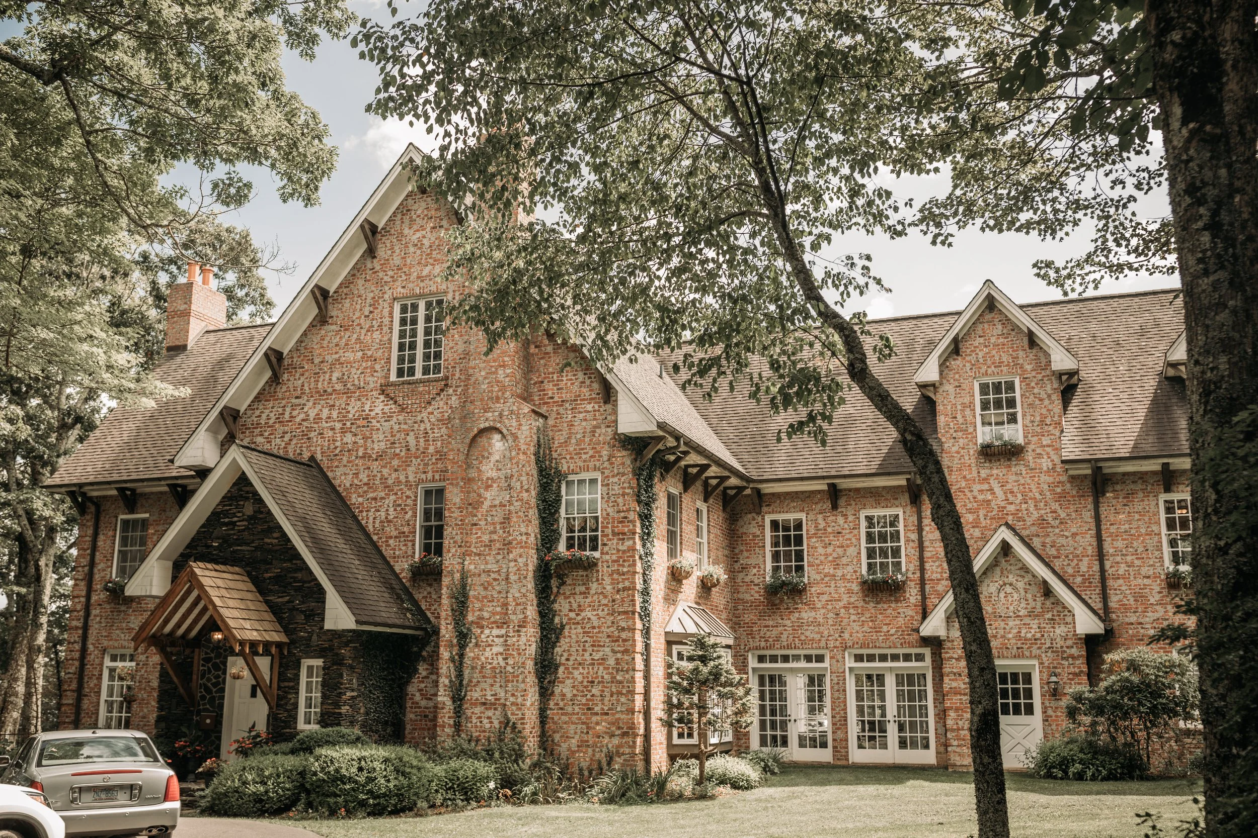 Historic brick estate wedding venue exterior surrounded by trees and landscaped greenery.