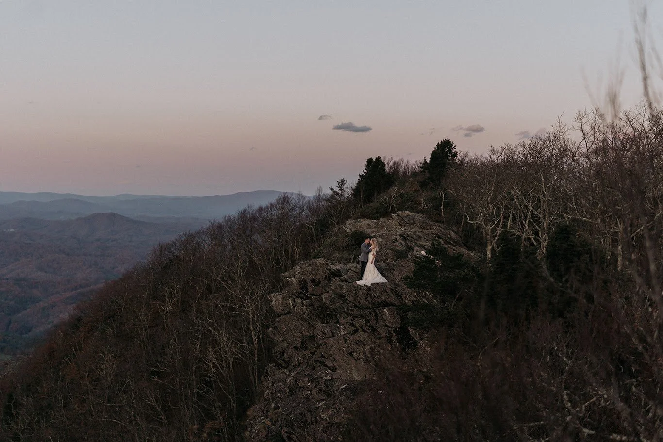 Wide landscape of a couple standing together on a rocky mountain ridge at dusk